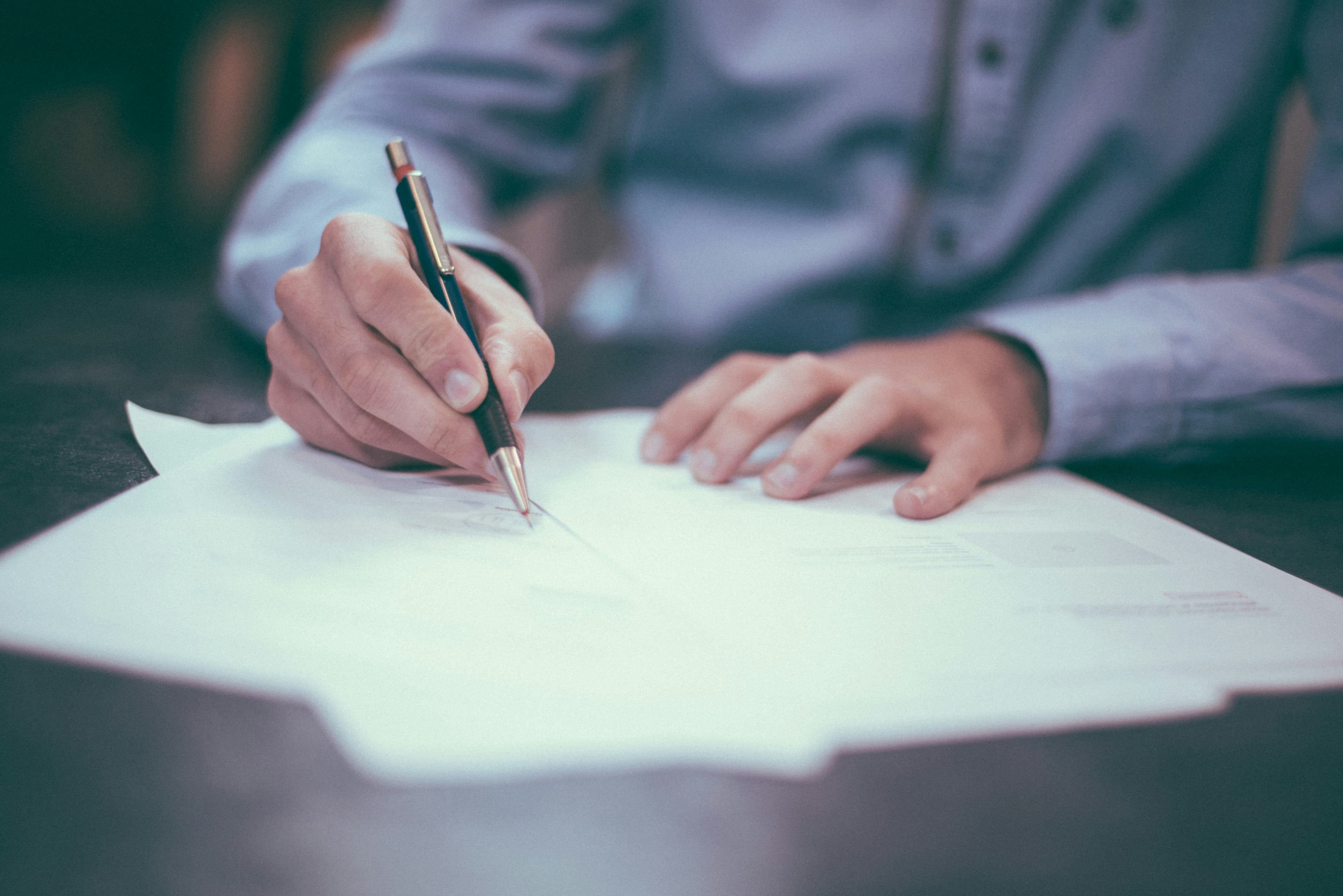 A person signing a document with a pen, representing exchange of contracts in a UK property sale