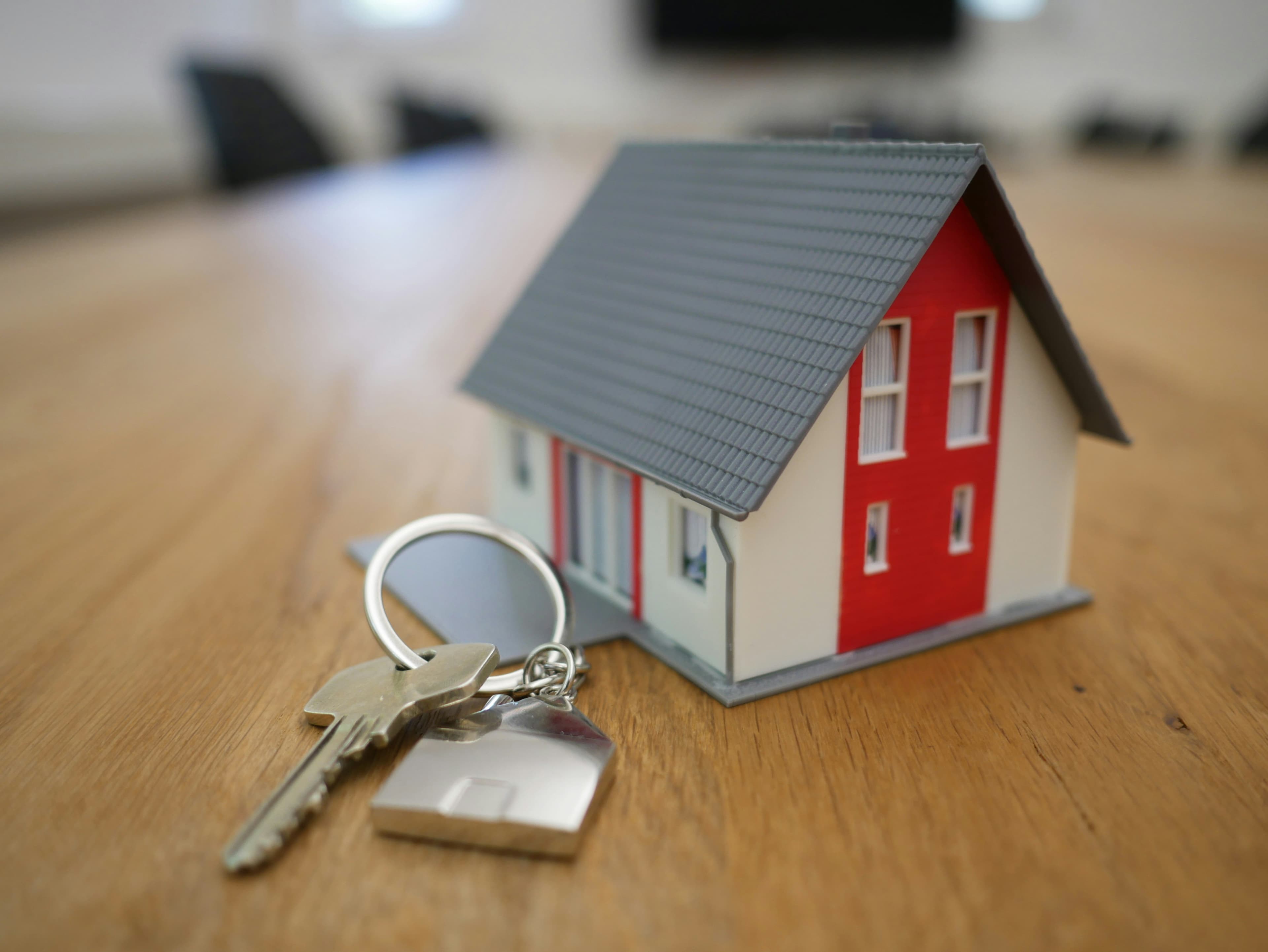 A miniature wooden house model on a desk, representing a homeowner weighing up an offer