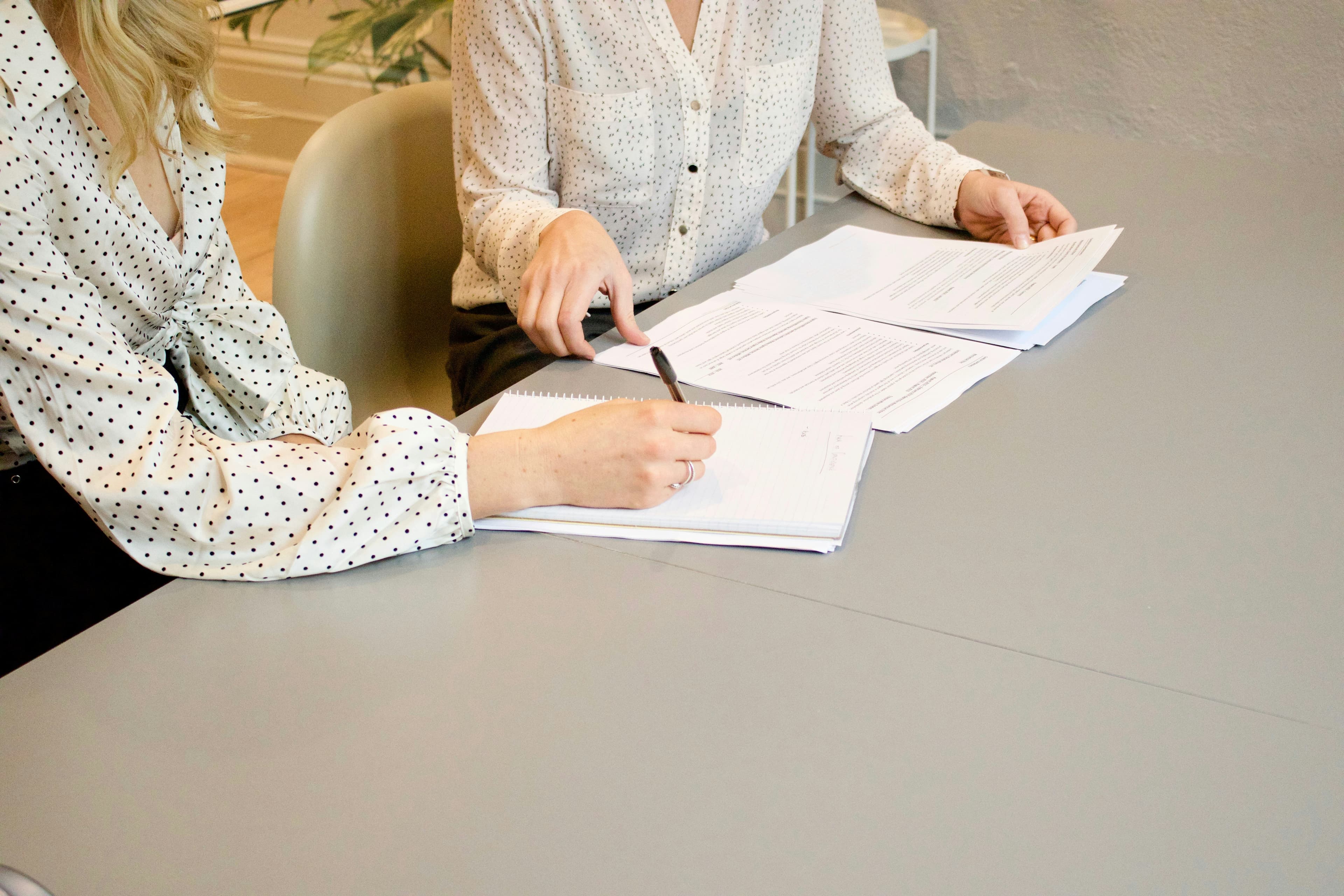 Two people reviewing and signing paperwork at a wooden table during a property meeting