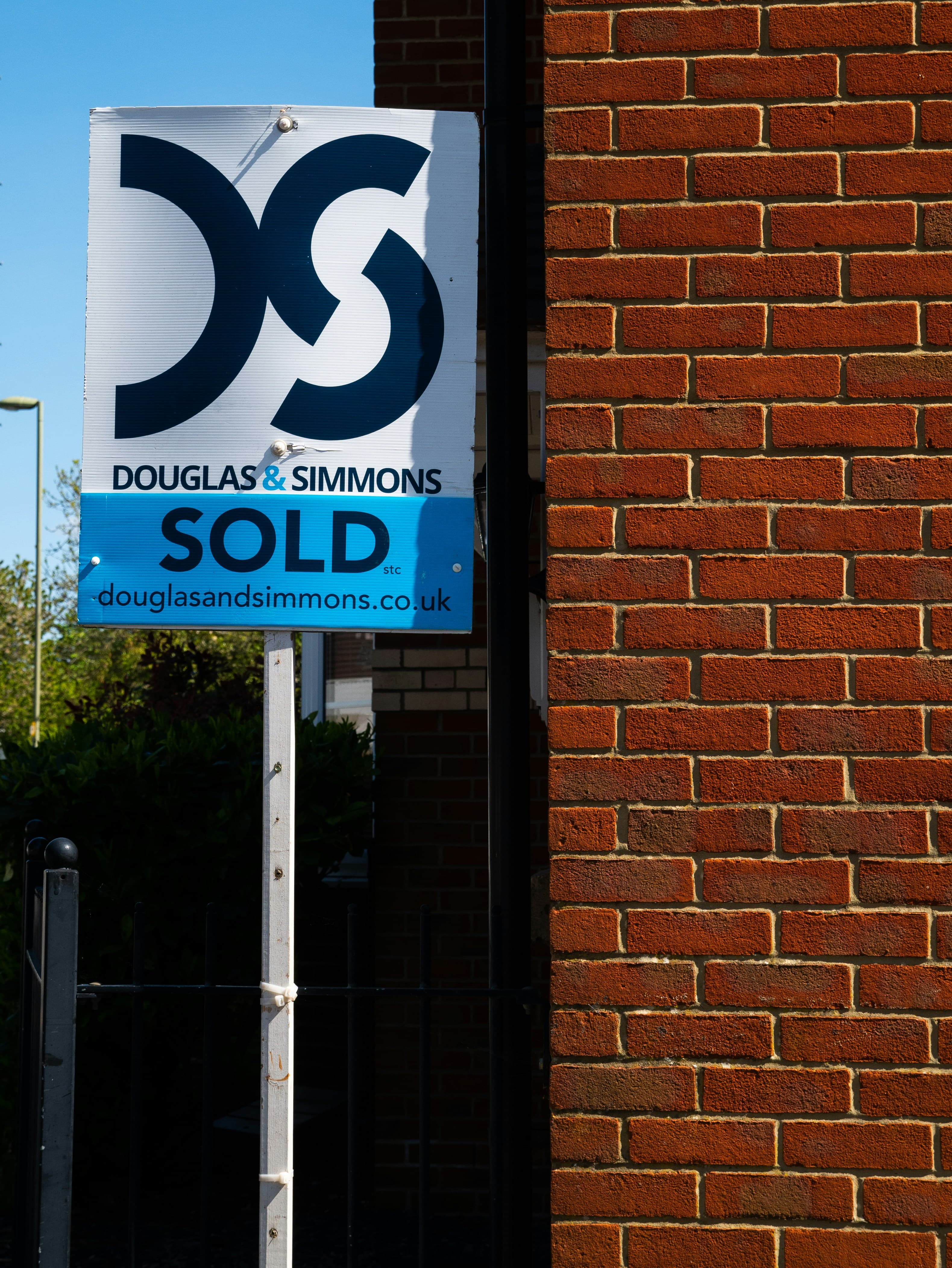 A UK estate agent board reading SOLD fixed to the red brick wall of a house.