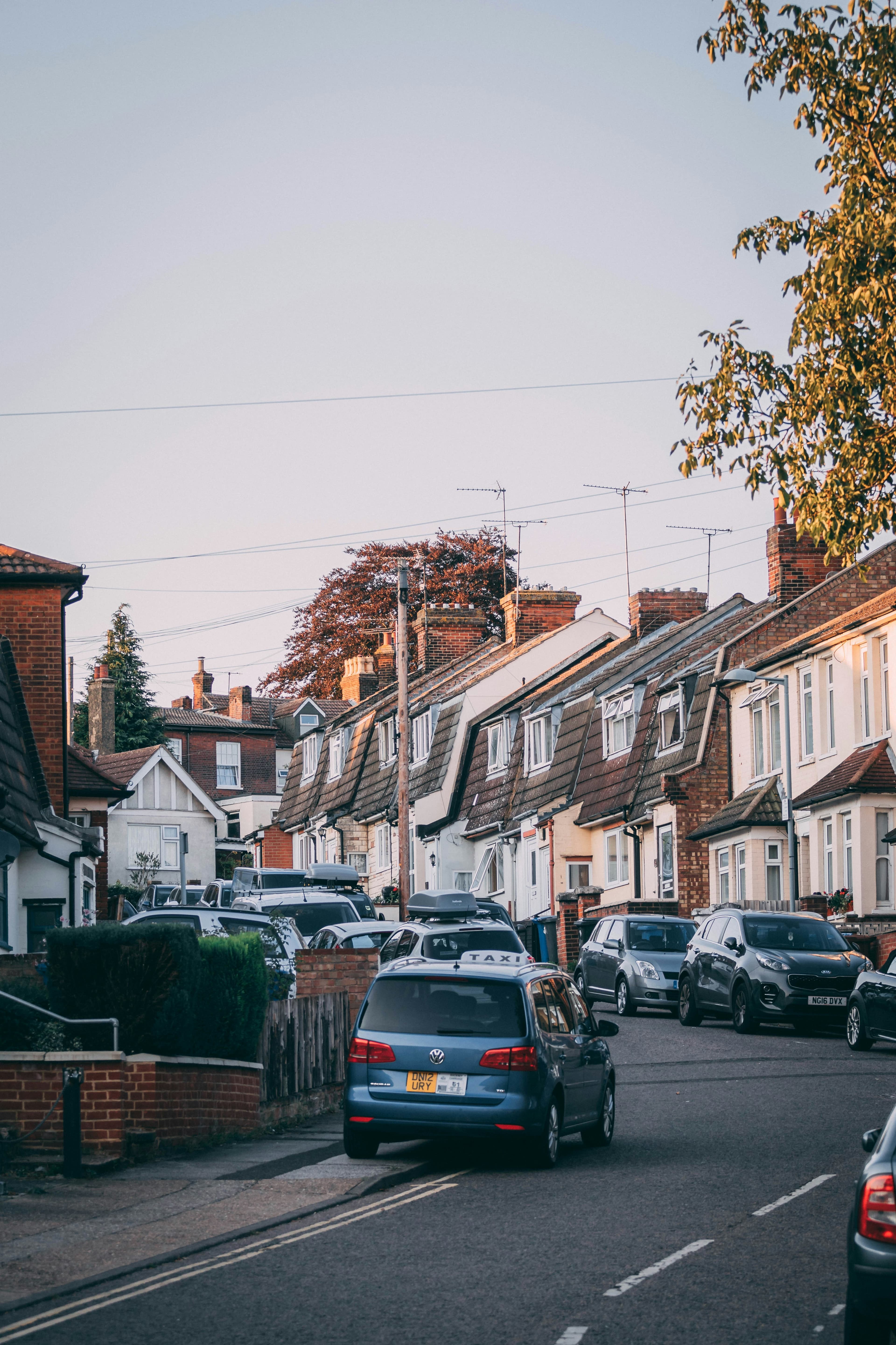 A row of brick UK houses on a residential street with cars parked outside
