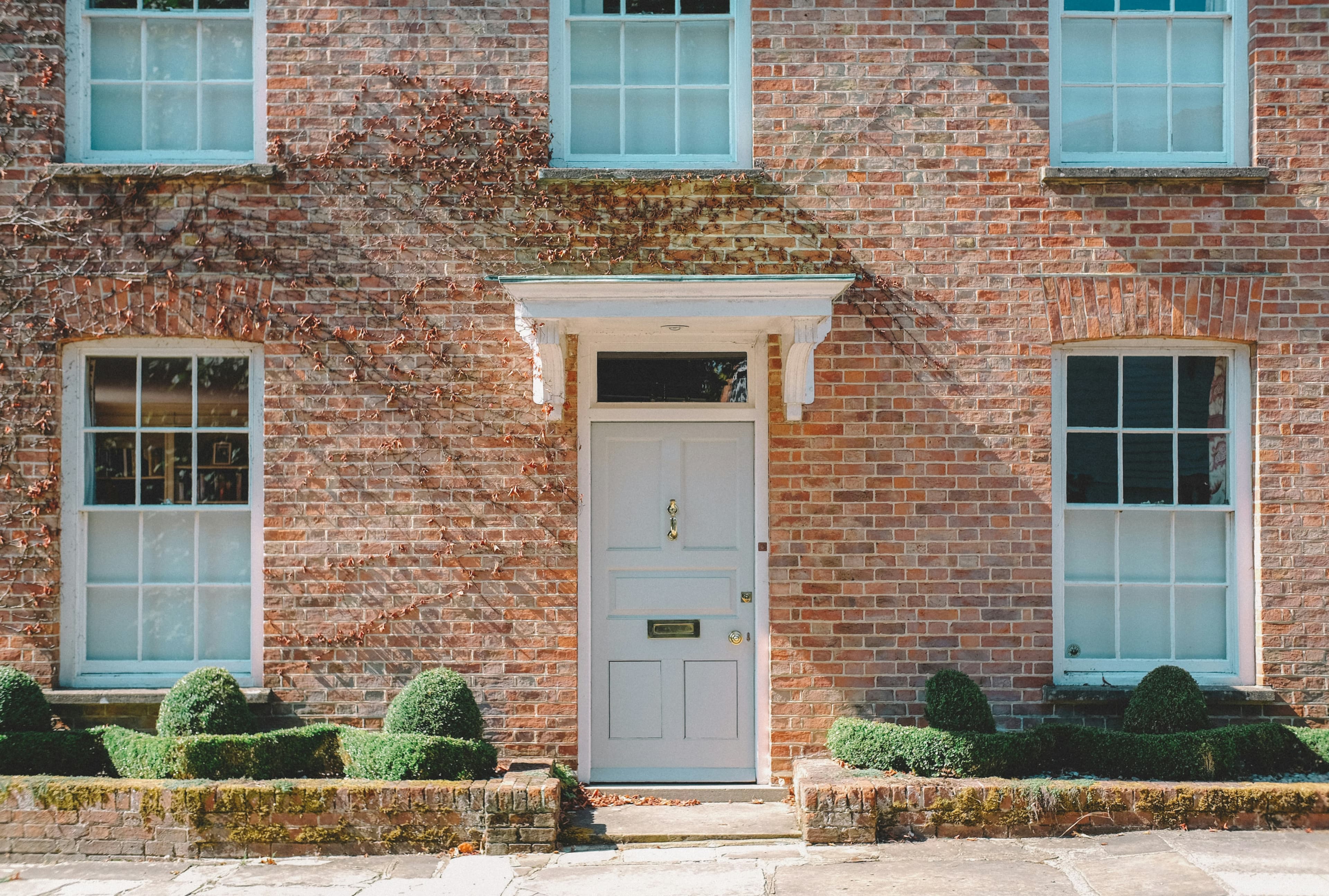 Brown-brick UK townhouse with a white wooden door, typical of suburban British residential streets.