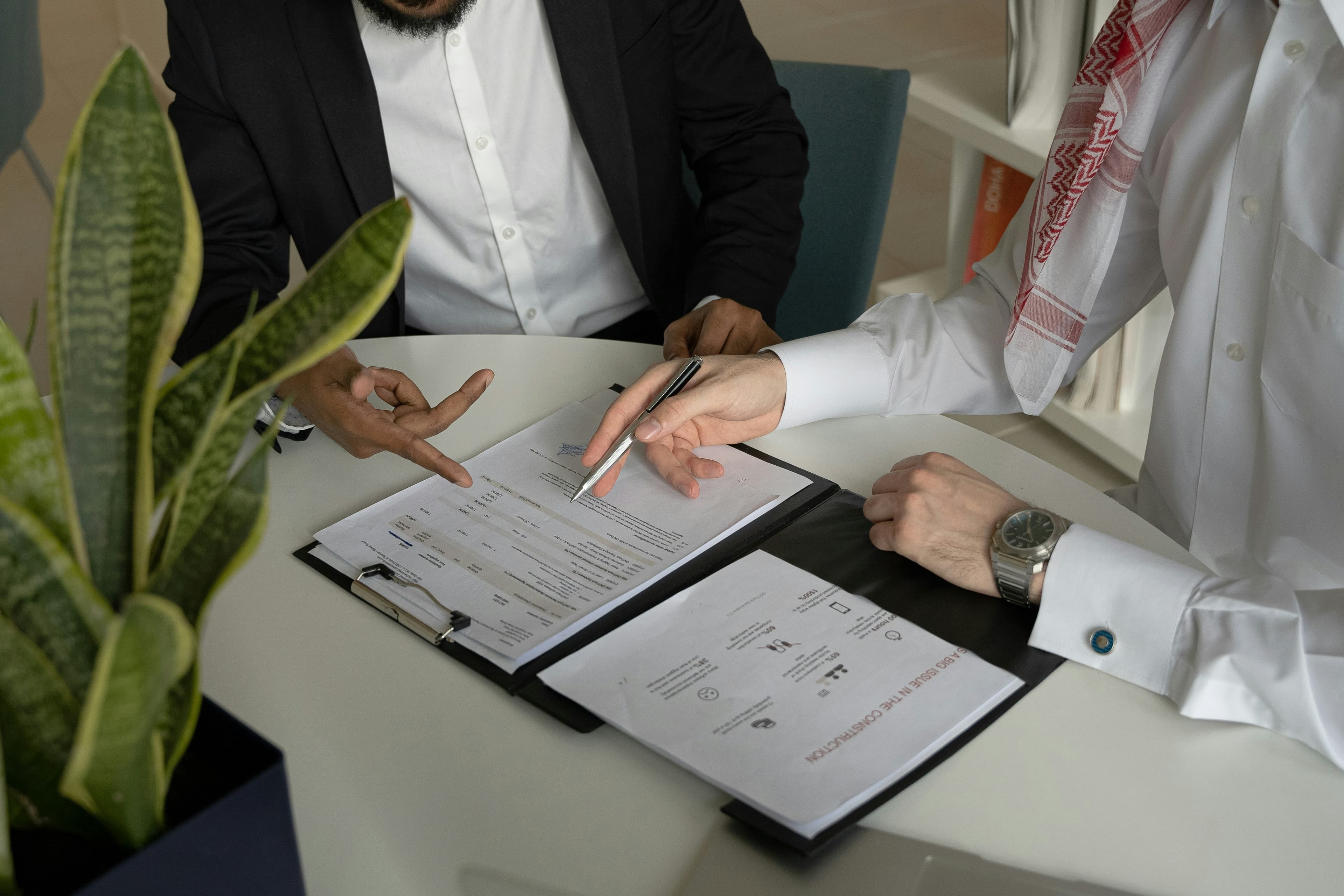 Two people sitting at a table with papers and a pen, reviewing a document