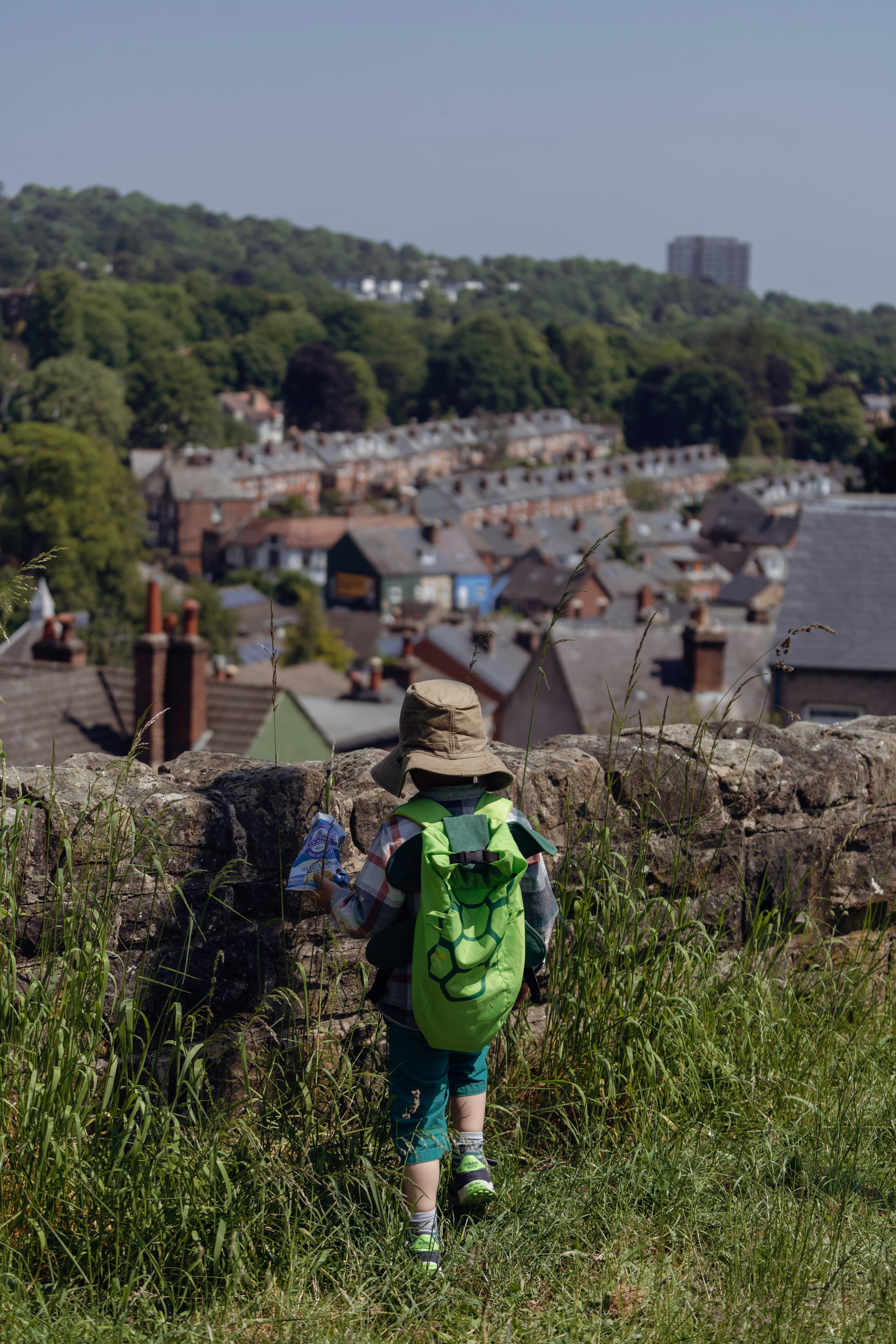 A young child with a green backpack walking up a hill on the way to school