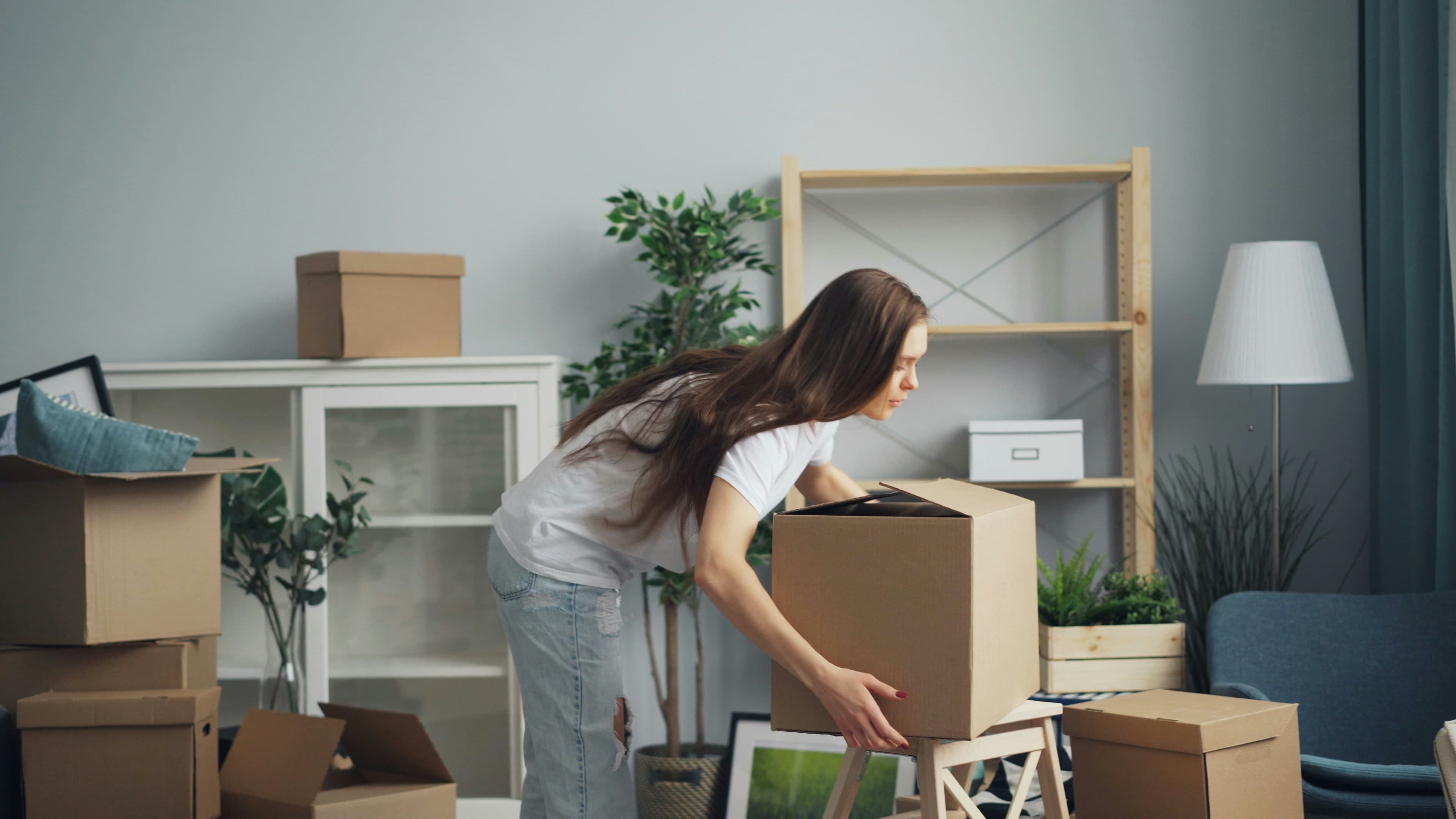 A person carrying cardboard moving boxes in a residential living room.