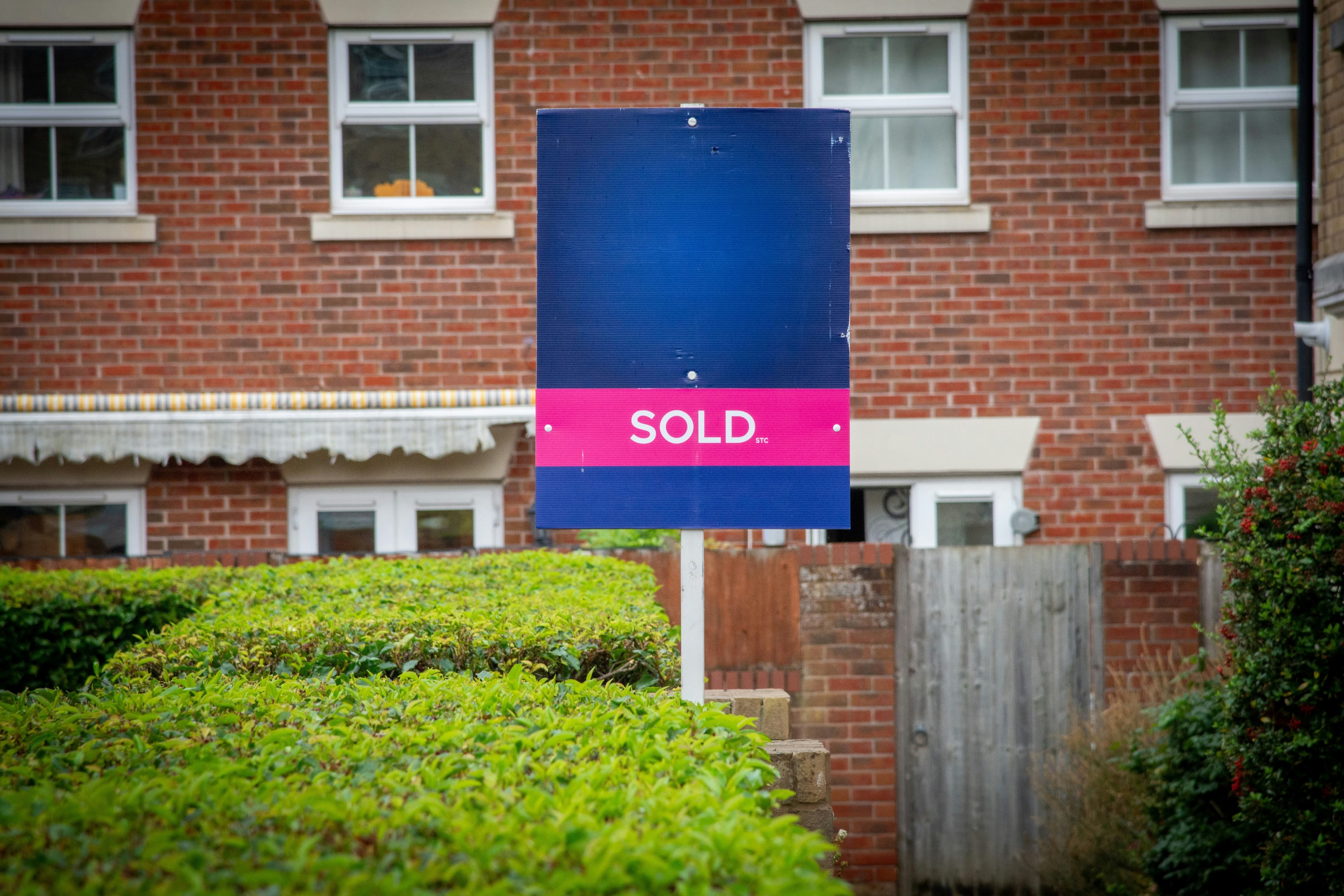 A SOLD board outside a UK brick house on a residential street