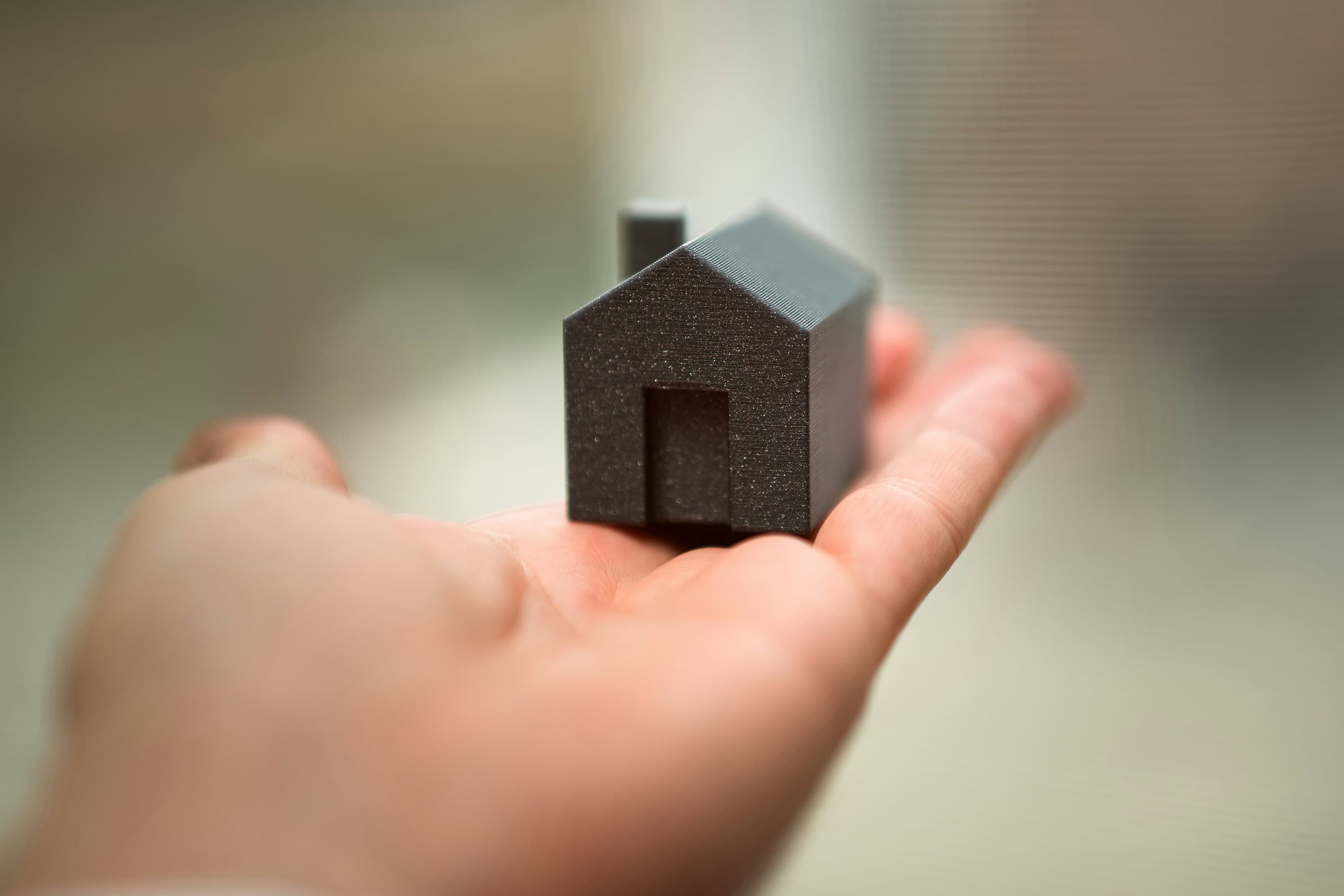 A hand holding a small model house, representing a buyer's commitment to a purchase.