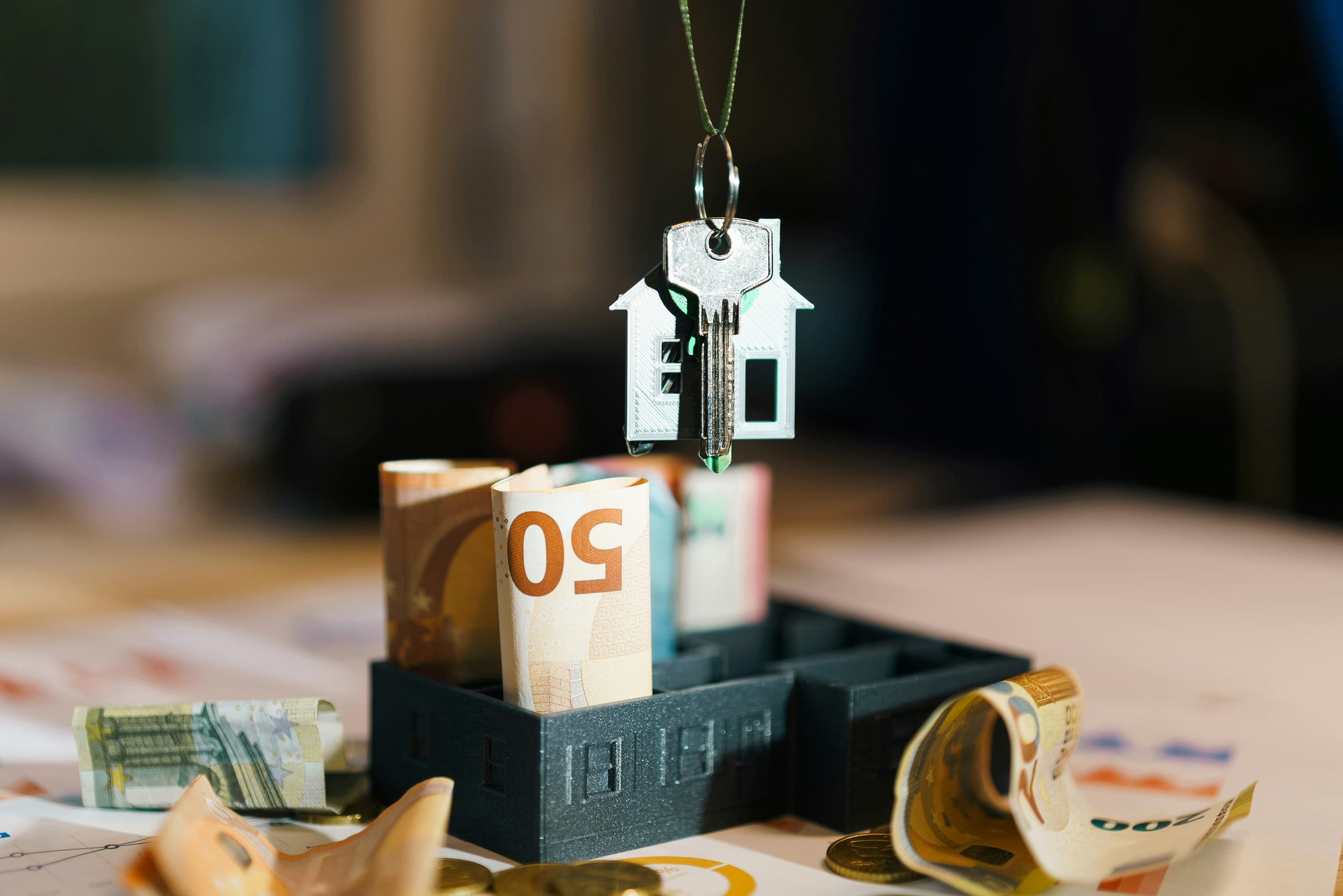 A small model house hanging on a string above a pile of banknotes