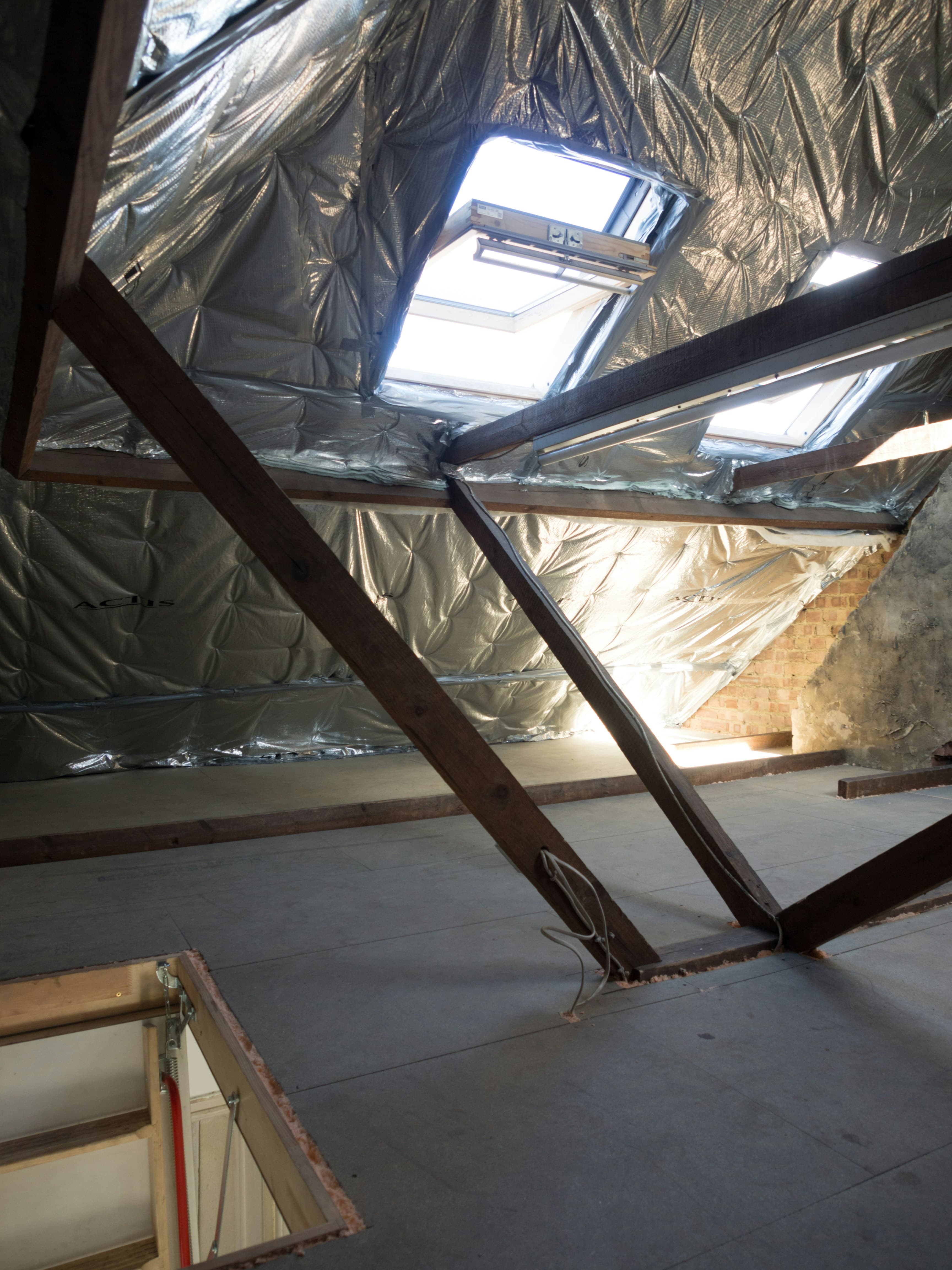 An attic space with insulation between wooden beams and a skylight
