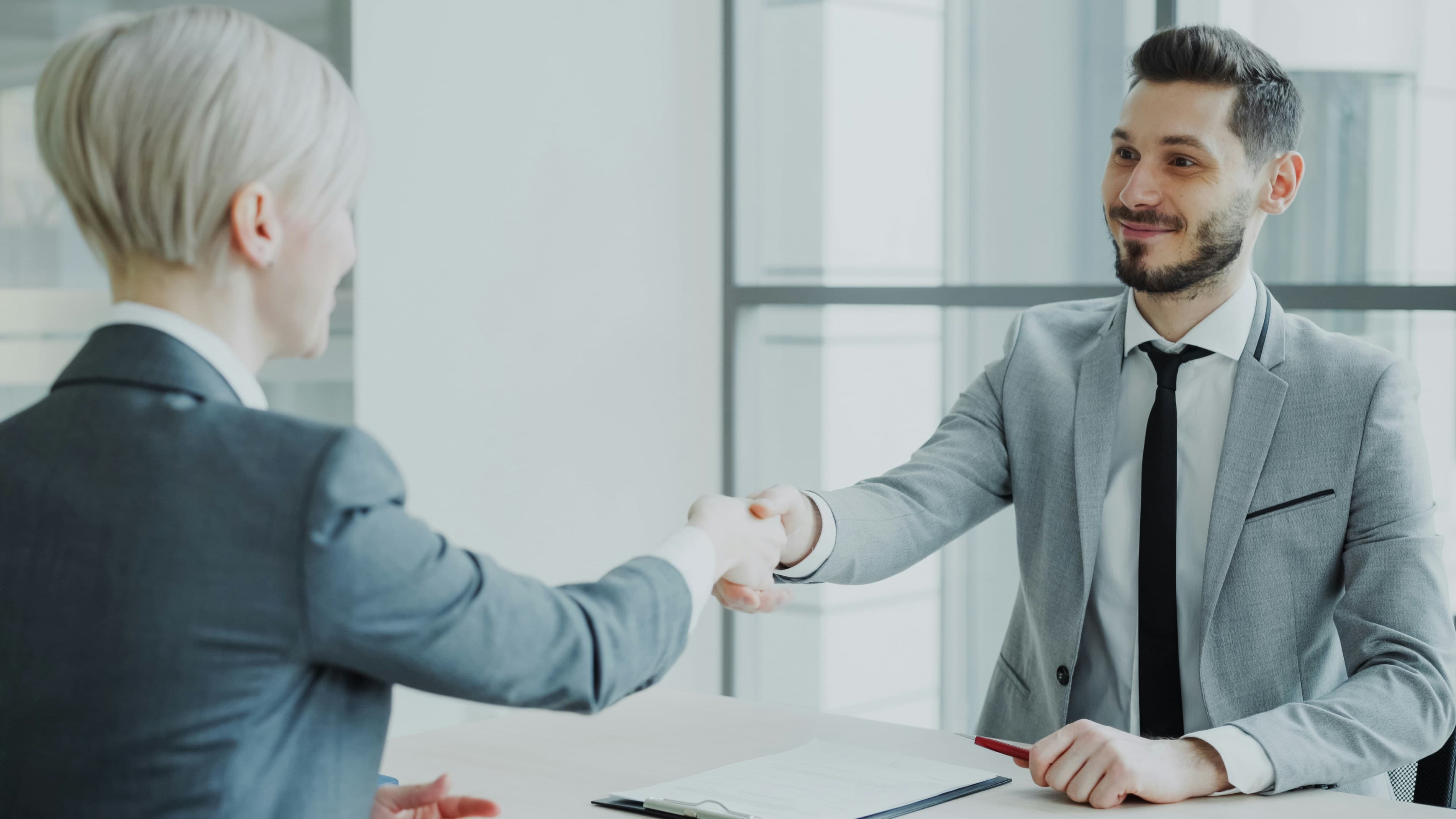 Two business professionals shaking hands across a wooden table, representing a property agreement.