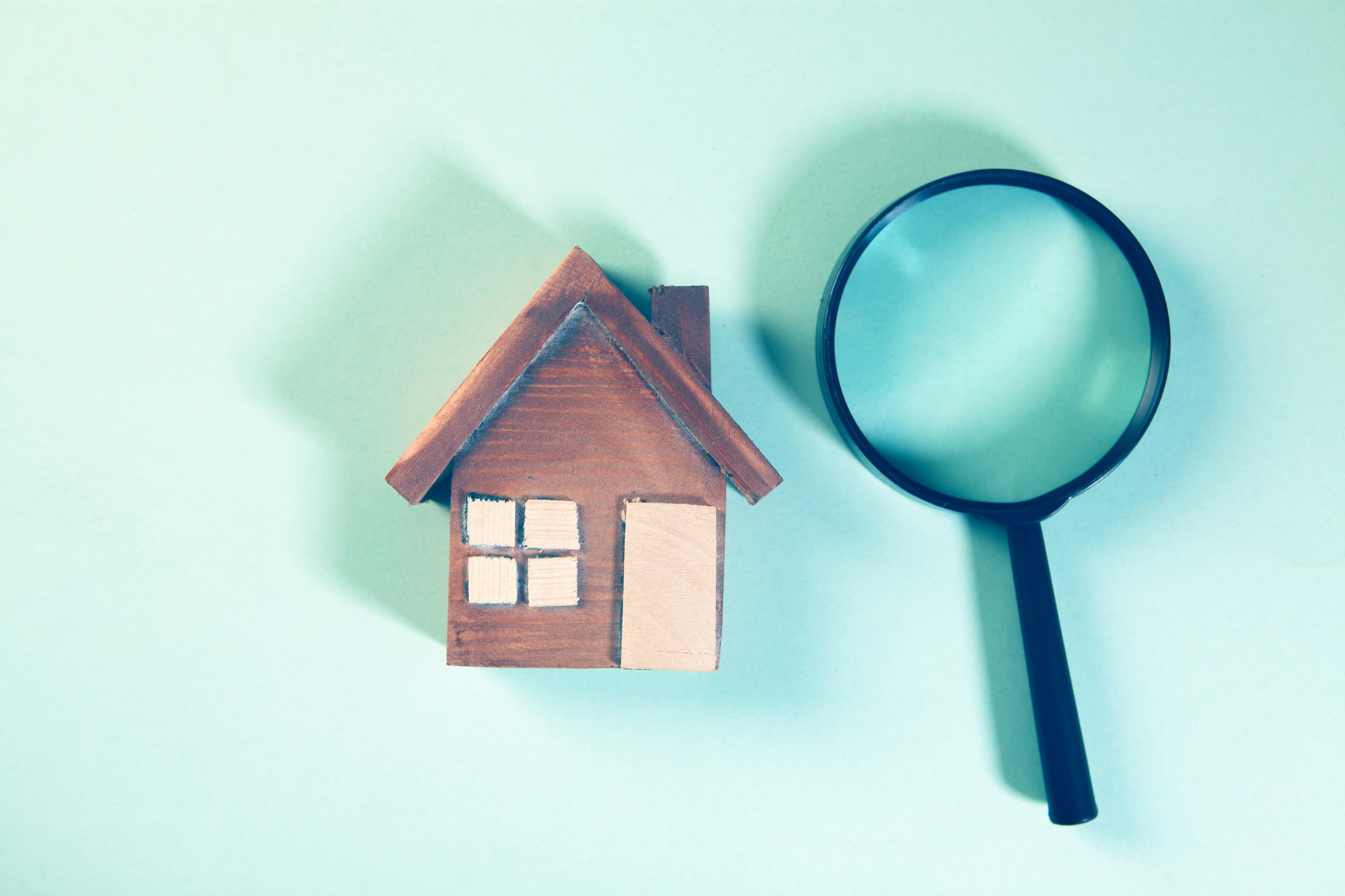 A magnifying glass positioned over a small wooden house model, representing a property inspection.
