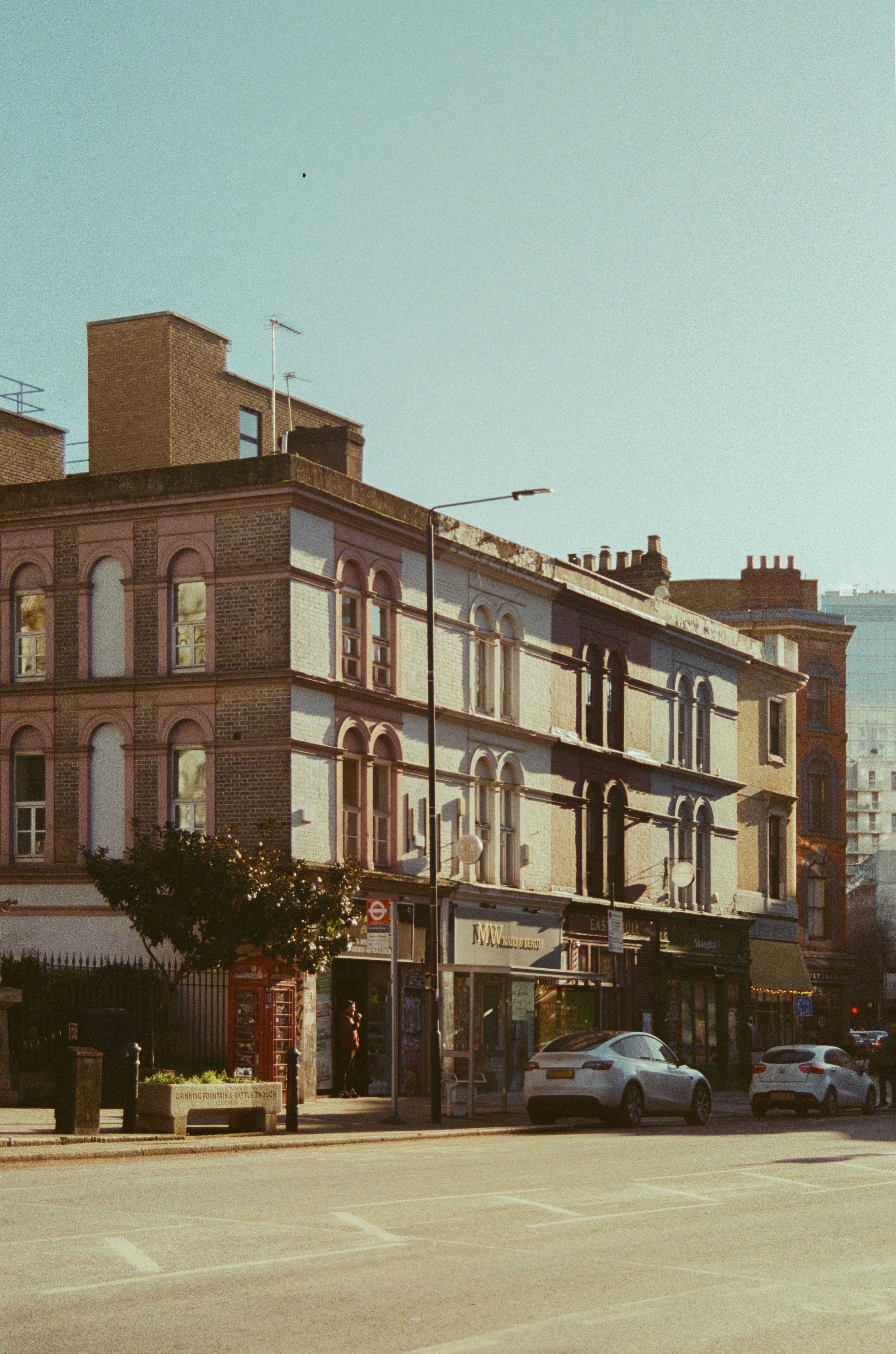 Row of UK shopfronts and residential buildings along a parked street