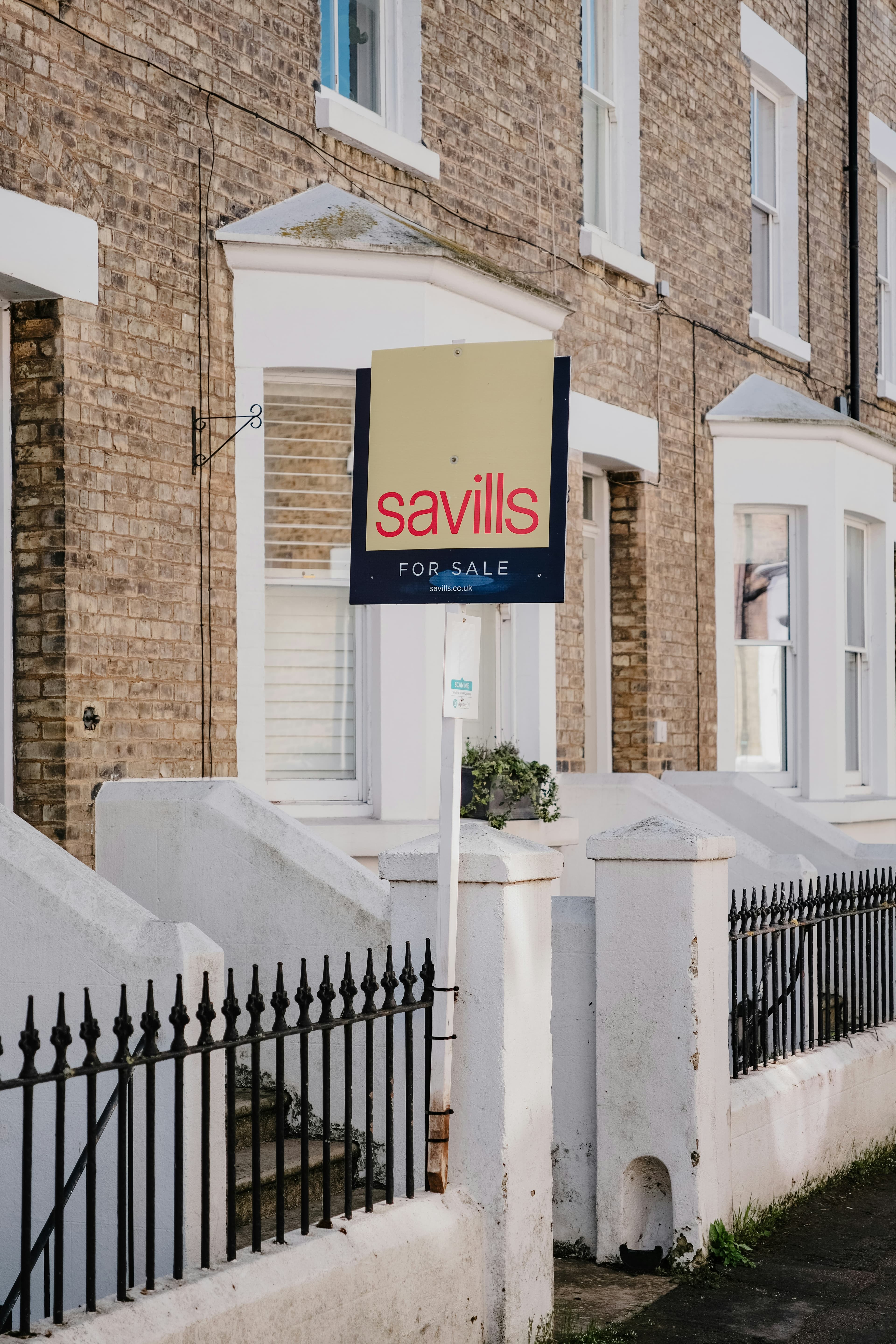 A Savills for sale sign outside a row of brick townhouses
