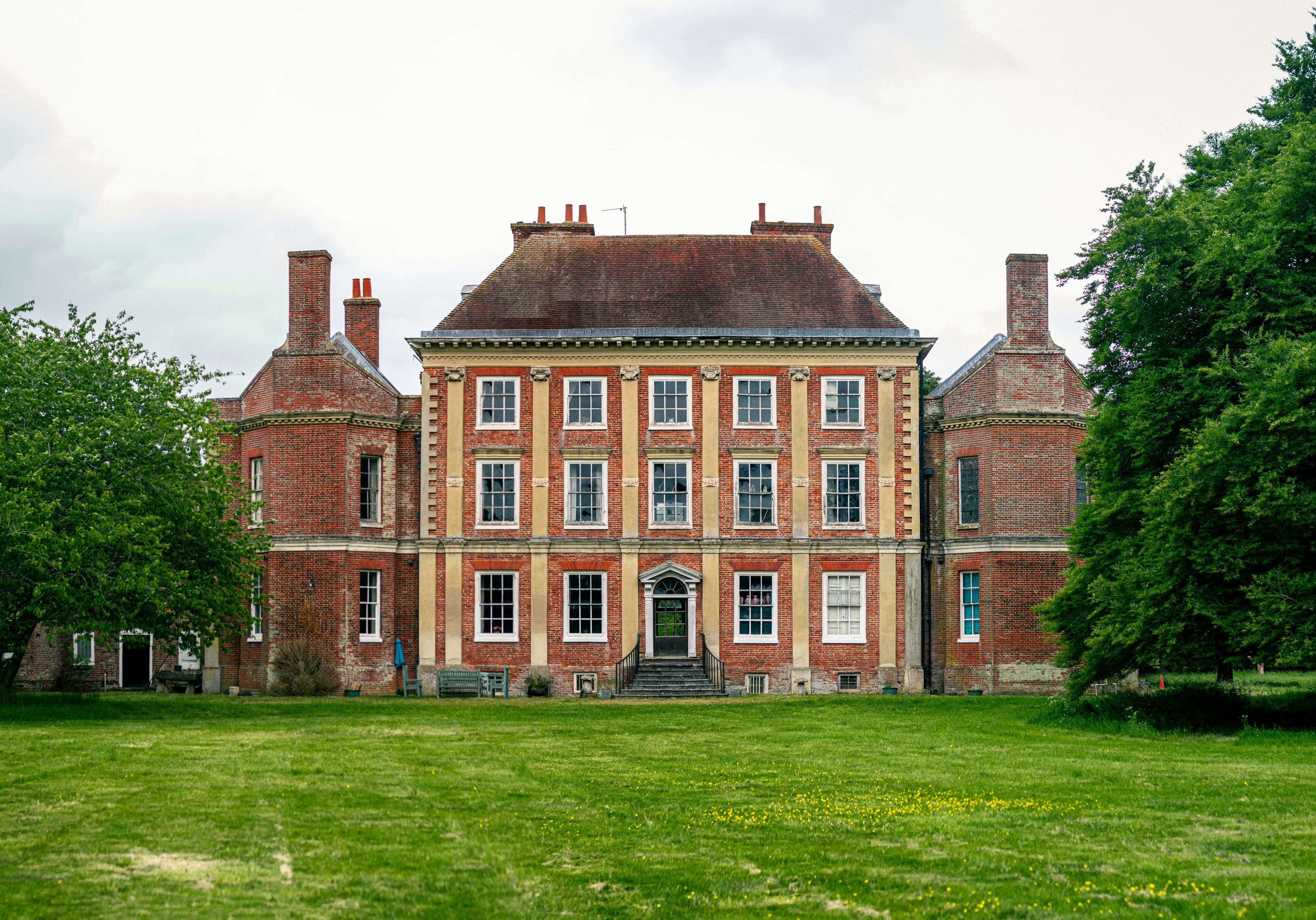 A grand red brick English manor house with manicured lawns under a clear sky