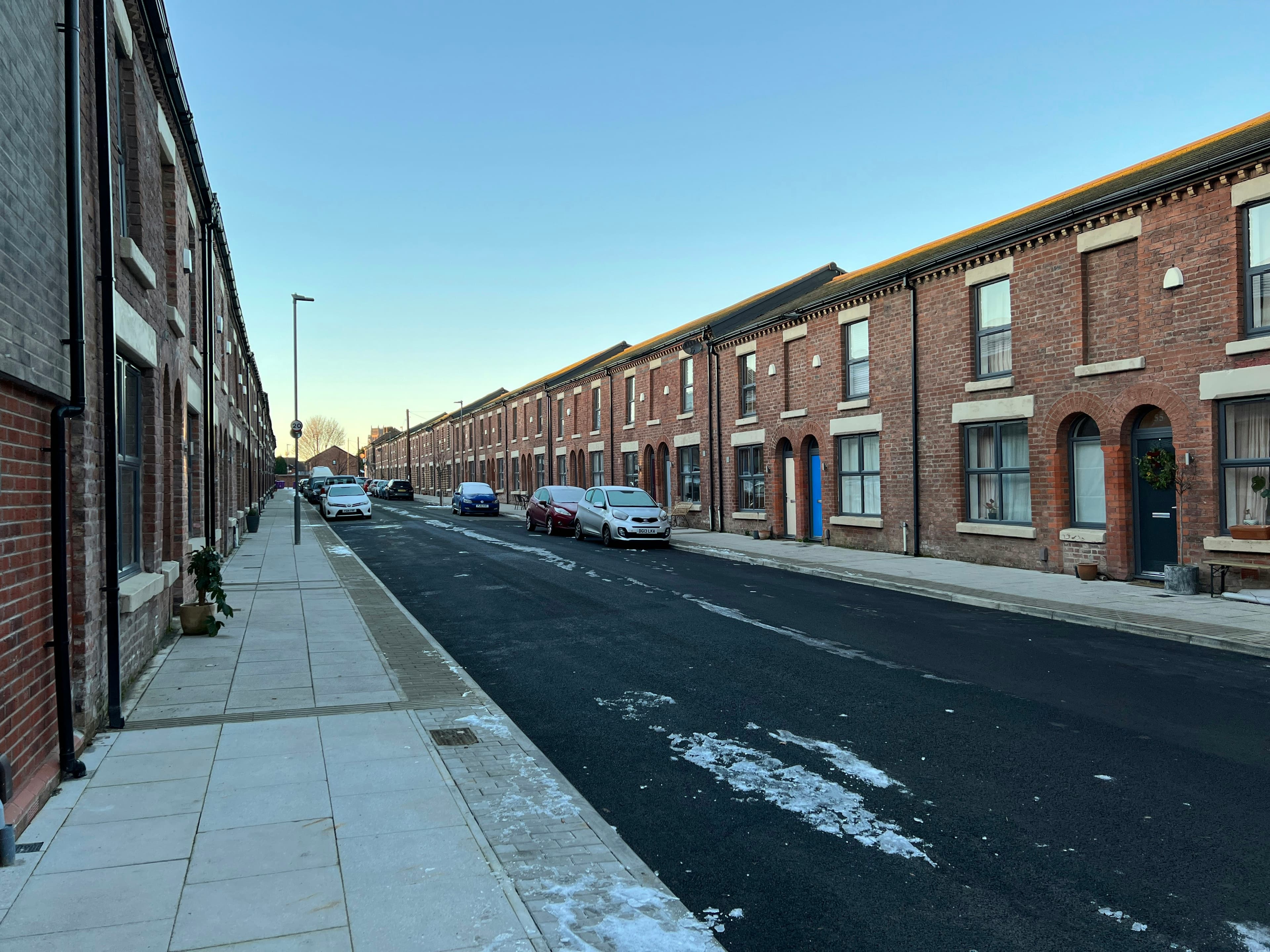 A street of brick terraced houses in England with cars parked along the kerb