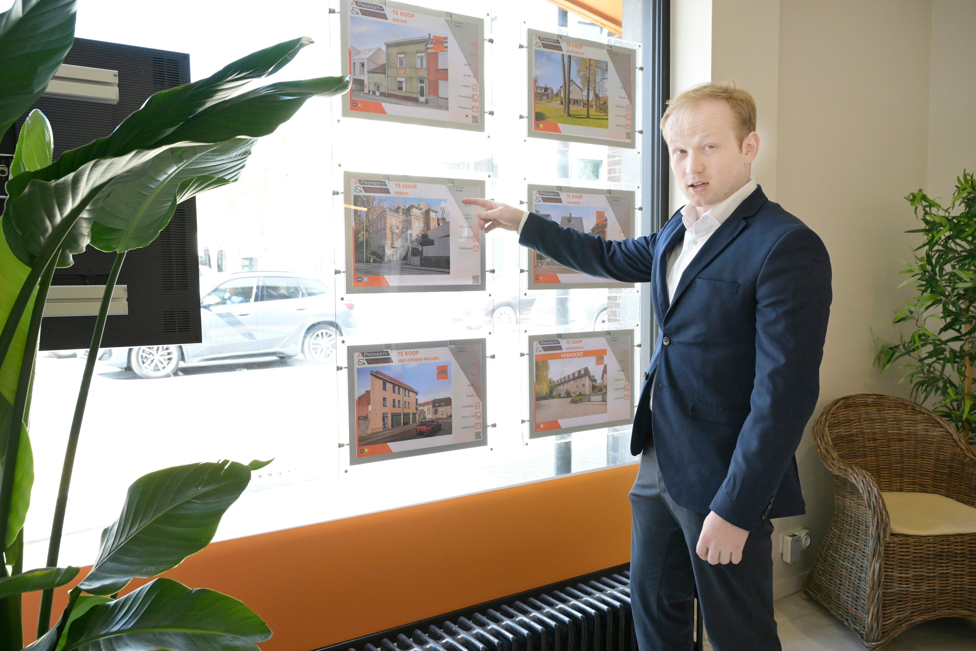 An estate agent points at property listings displayed in an agency office window