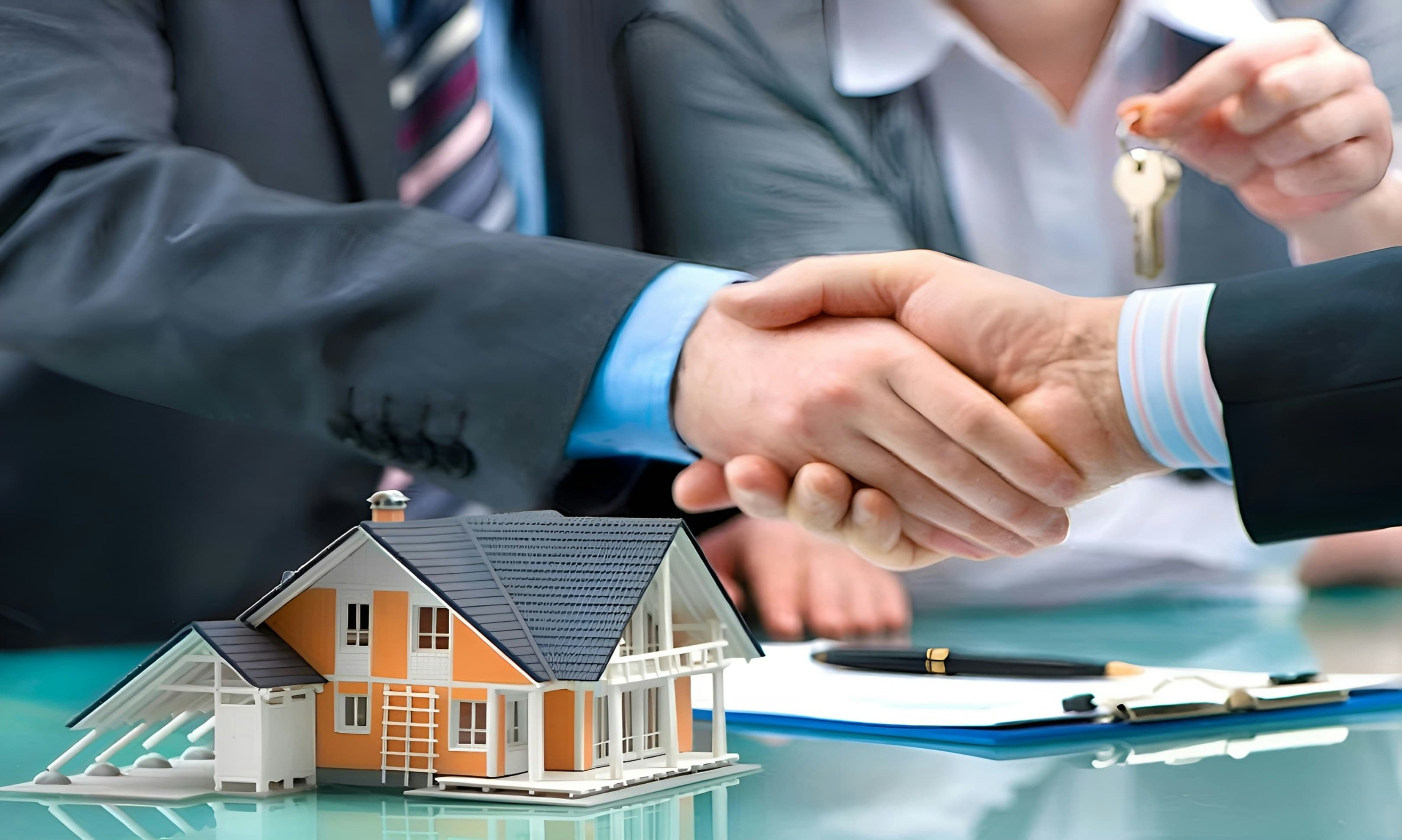 Two people shaking hands across a table with a model house and a set of keys
