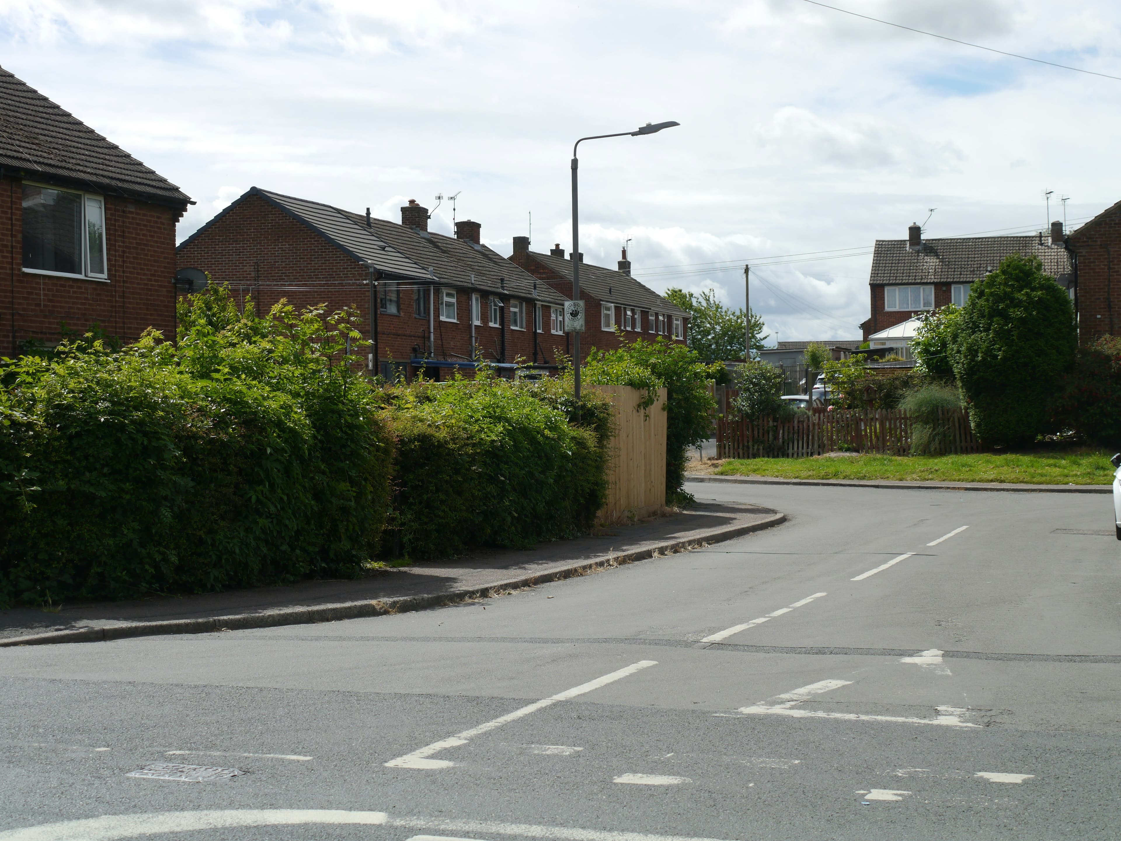 A quiet residential street of red-brick semi-detached houses with hedges and a cloudy sky