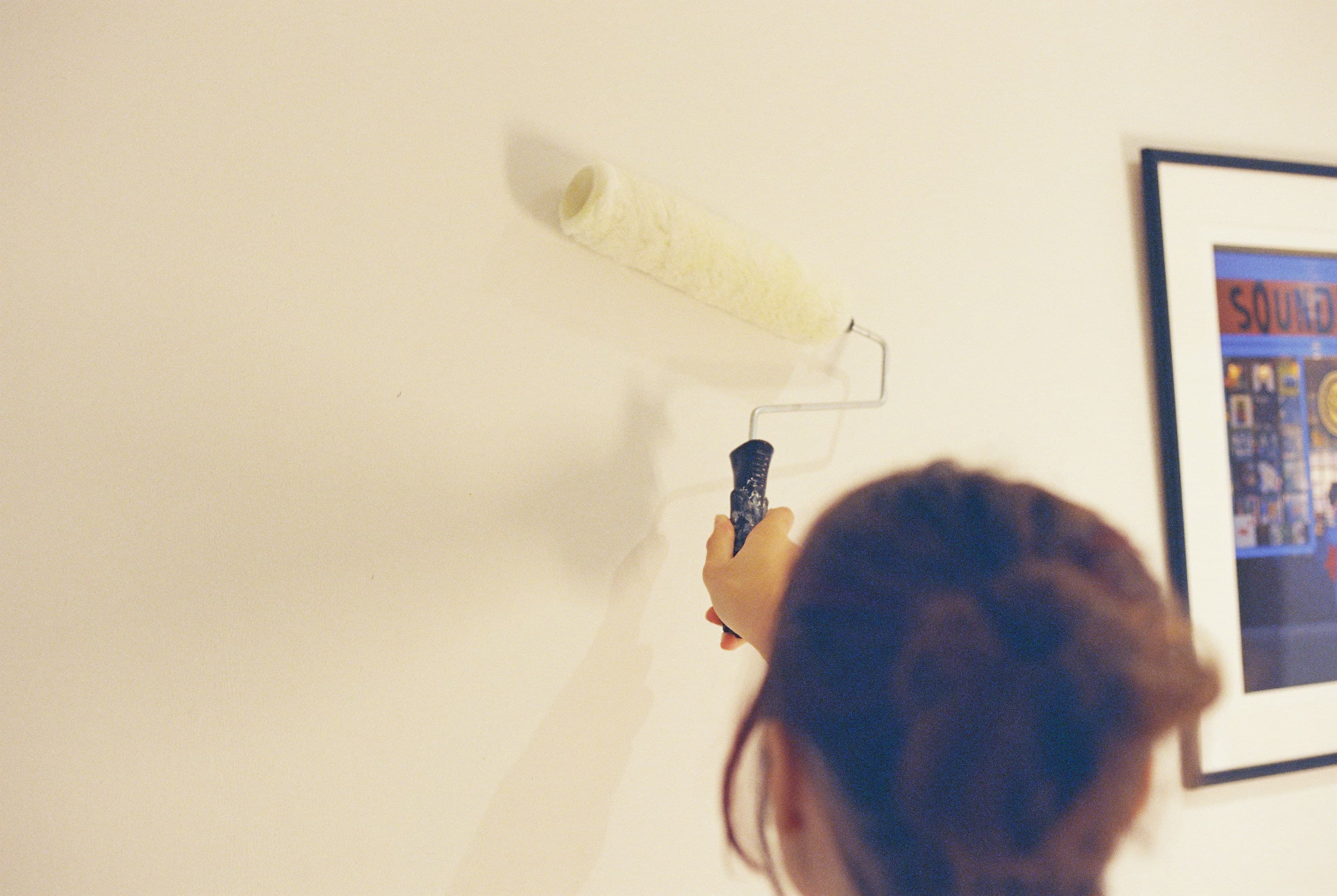 A person painting a pale wall with a roller beside a framed picture