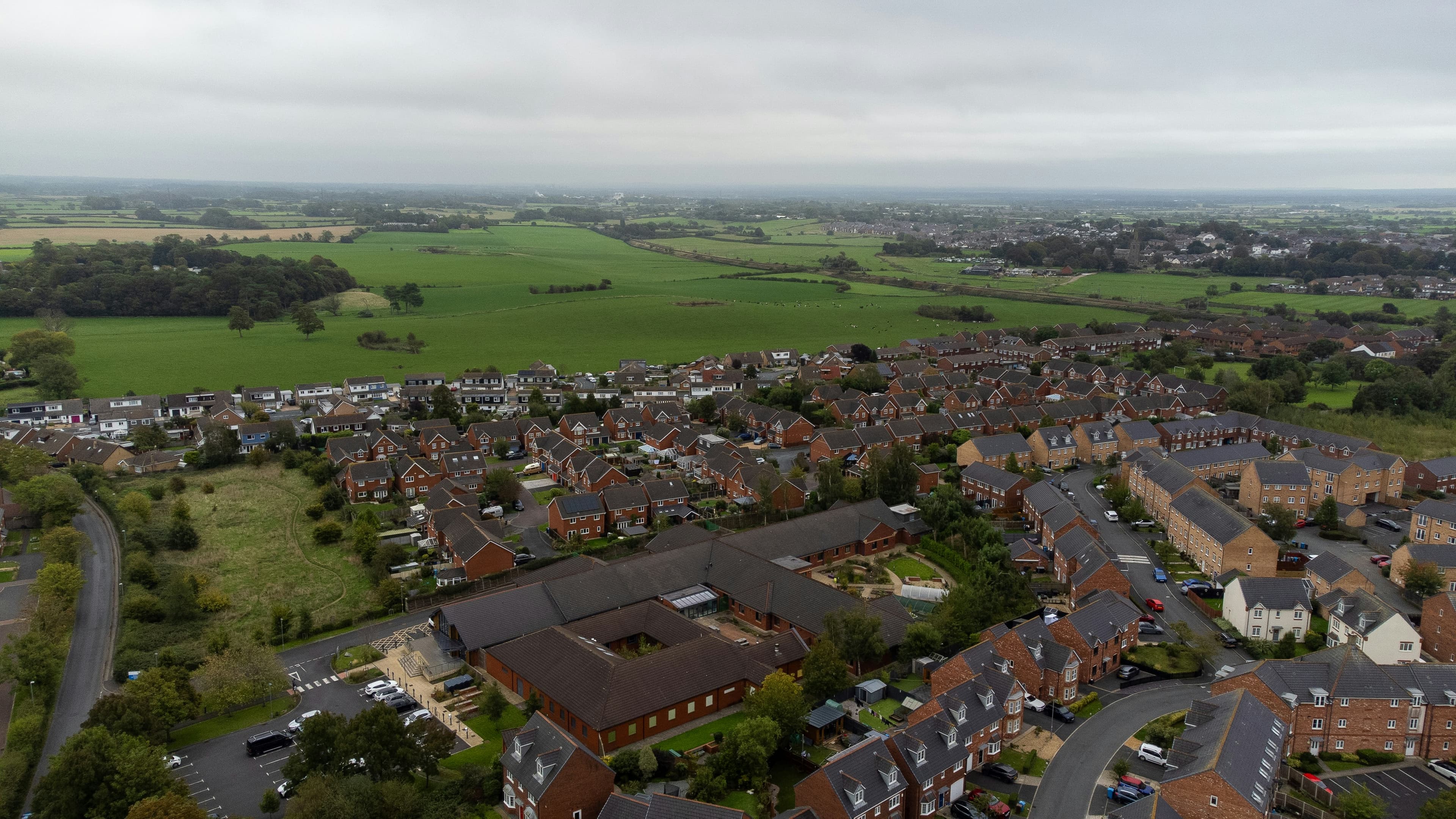 Aerial view of a brick housing estate of semi-detached and detached homes bordering green fields in England