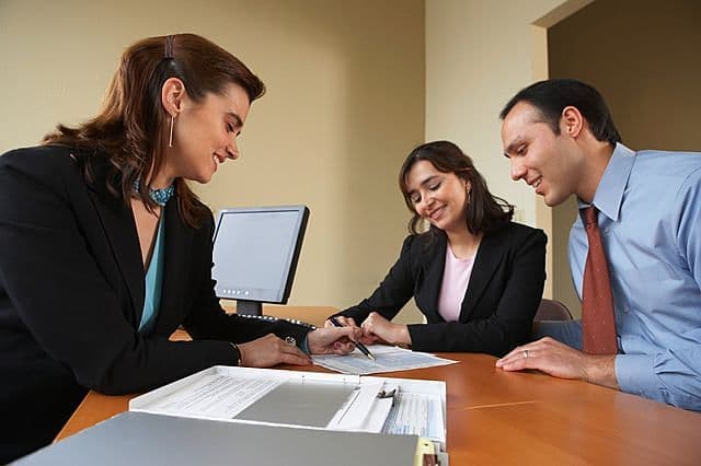 A couple sitting across a desk from an estate agent in an office, discussing paperwork.