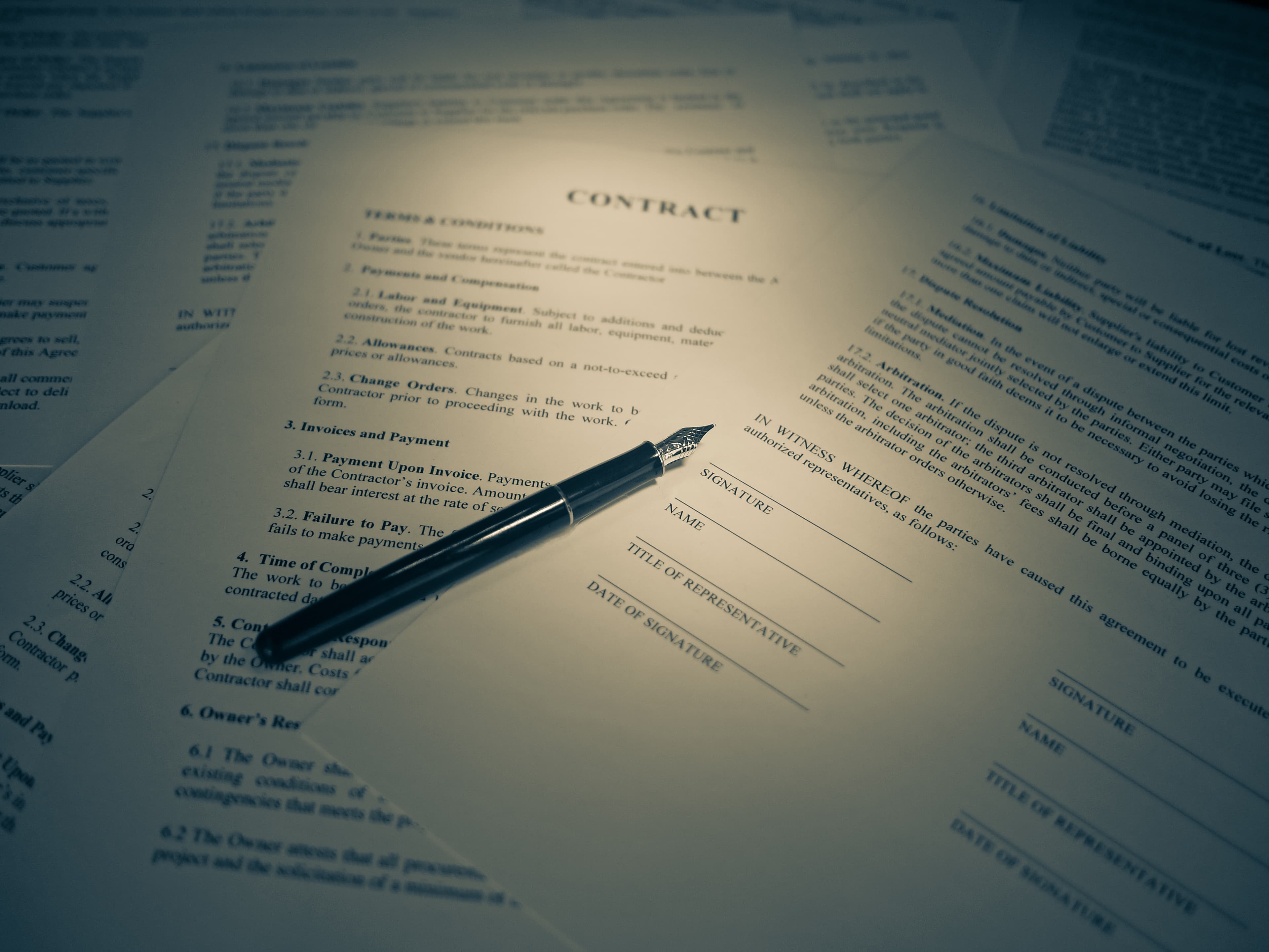 A hand signing a legal contract with a pen on a desk in warm light.