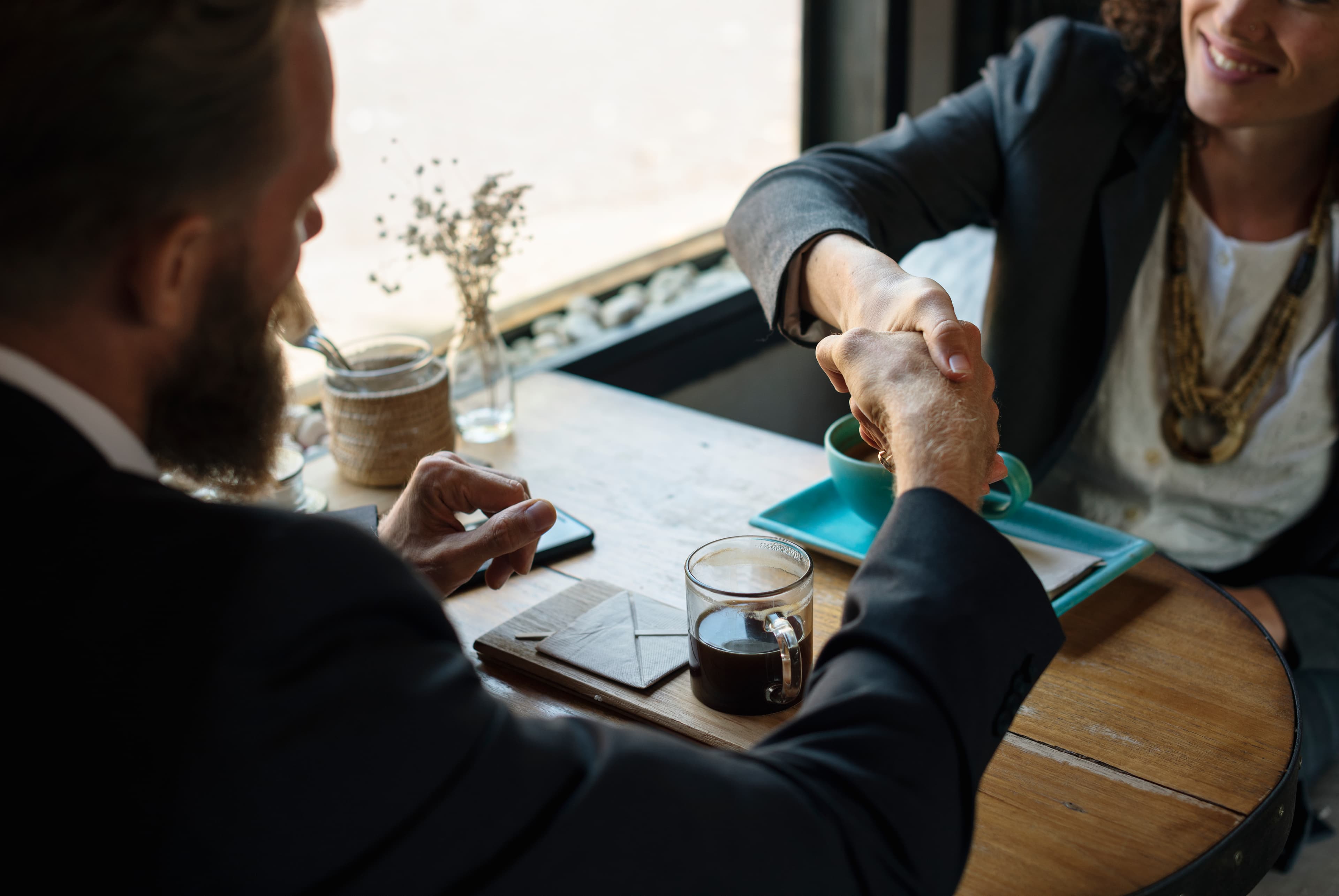 Two people shaking hands across a table to agree a deal