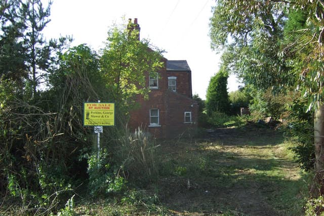 A brick house with an auction board outside it, awaiting sale