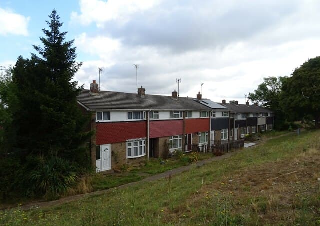 A row of terraced houses with red-tiled and grey frontages running along a grass bank beside the B1007 in Basildon, Essex