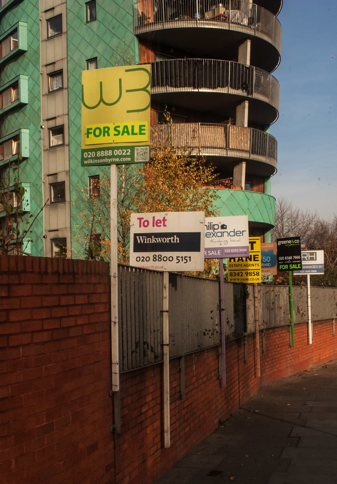Several estate agents' For Sale boards clustered together on a residential street