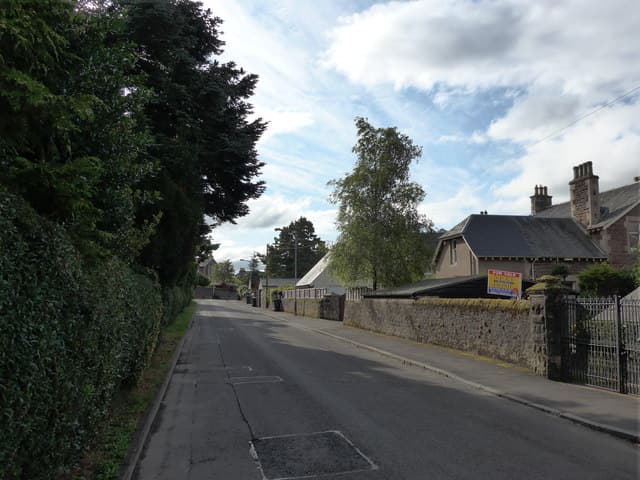 An estate agent's for sale sign outside a row of terraced houses on a residential street