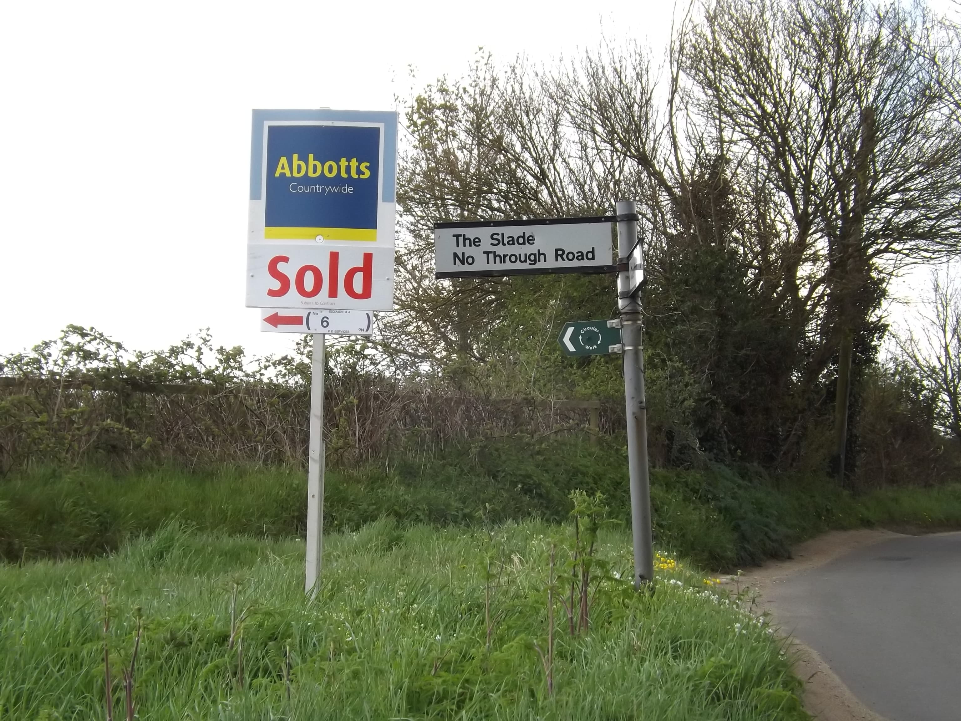 An estate agent for sale board mounted on a post beside a road outside a UK property