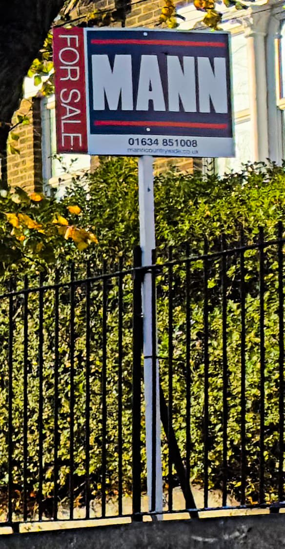An estate agent for sale board outside a house on an English street