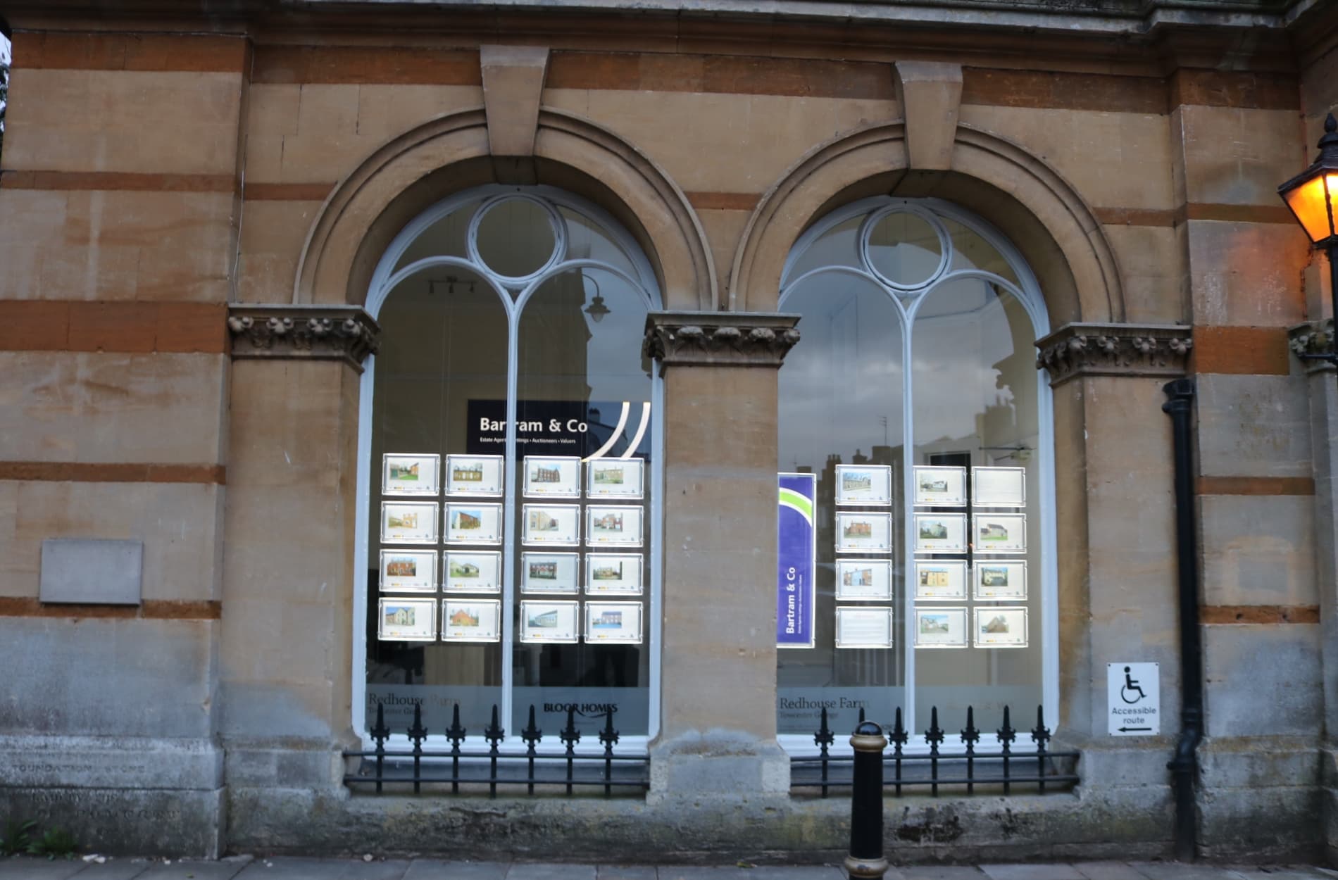 Arched windows of an estate agent's office in a stone building in Towcester, with rows of property listings displayed behind the glass