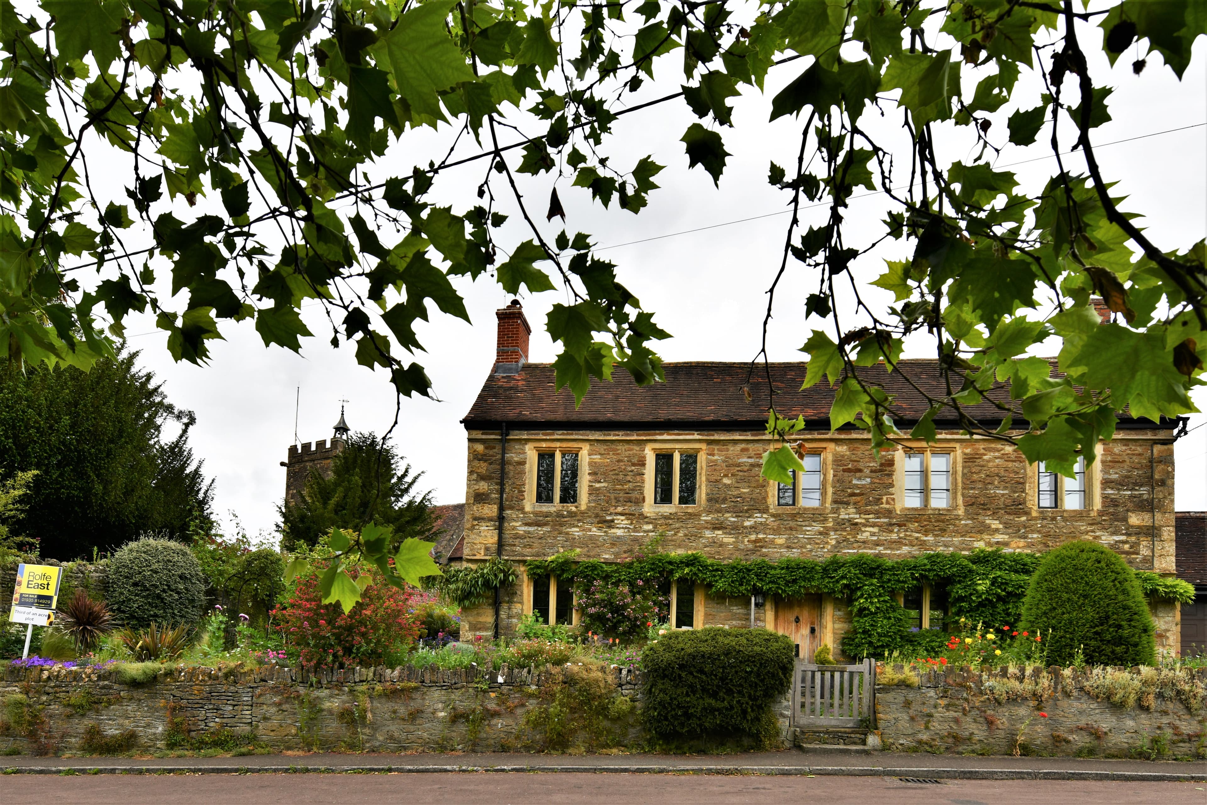 A large detached house with a for sale board outside it on a residential street