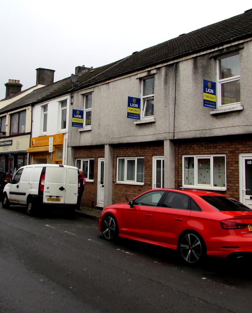 Three estate agent for sale boards standing outside terraced houses on a residential street
