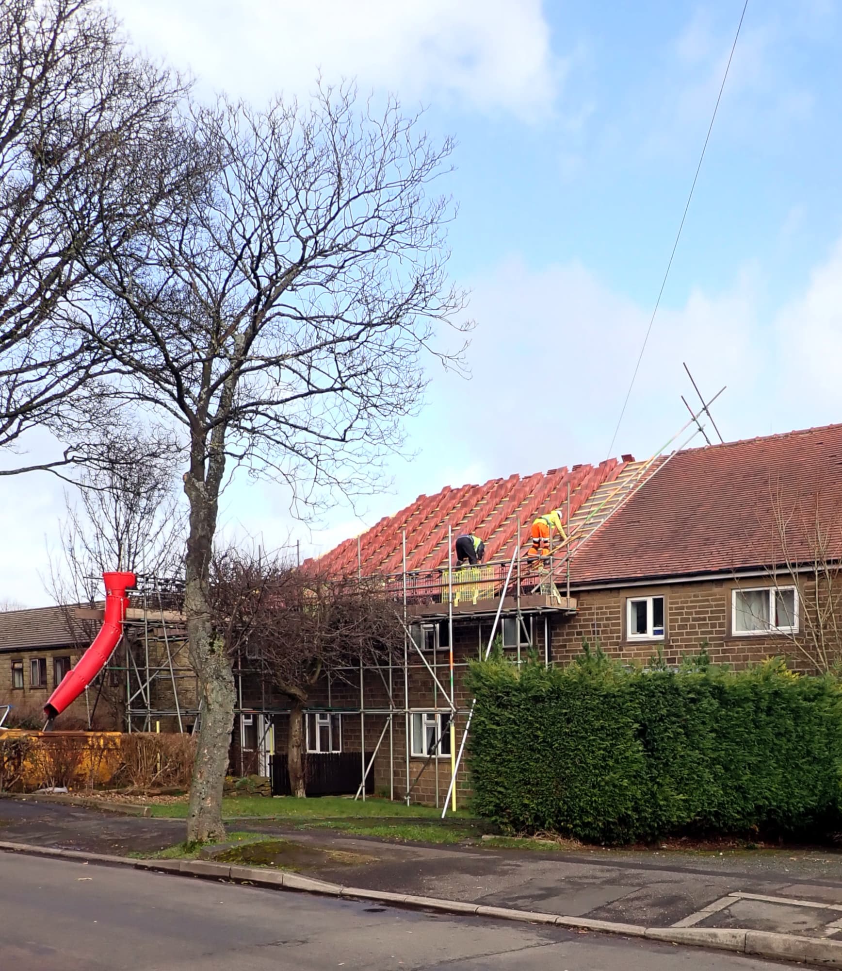 Roofers in hi-vis jackets working on scaffolding as they re-tile the roof of a row of stone houses on a residential street