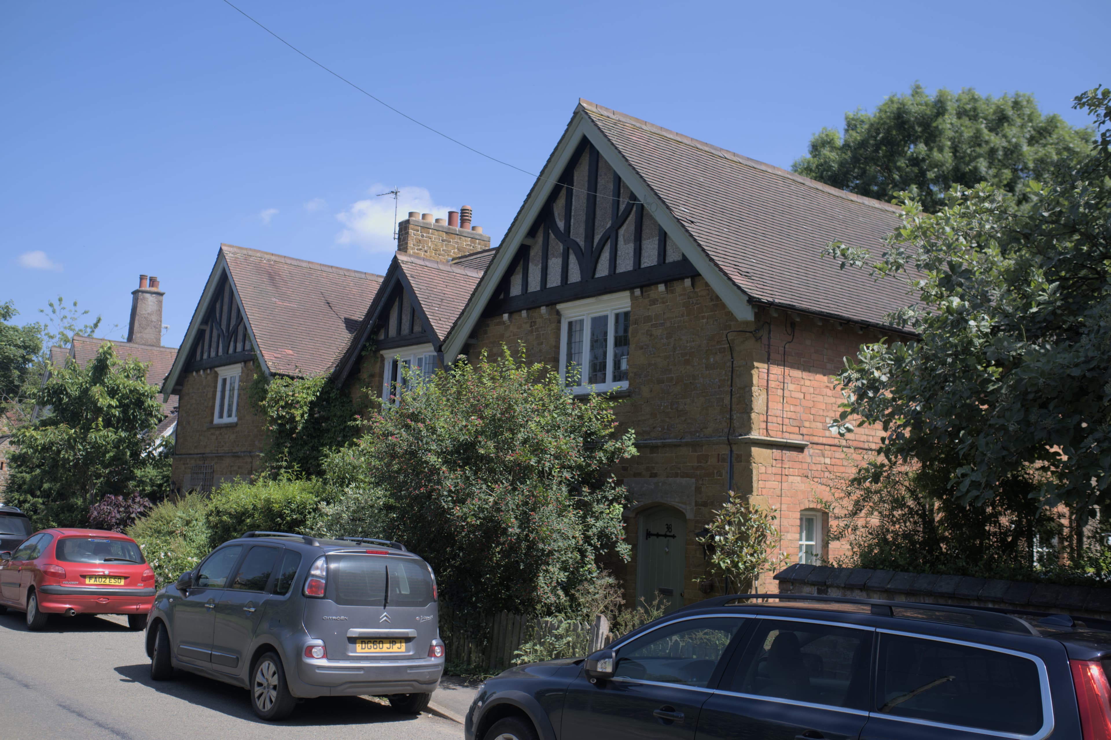 A row of brick Edwardian houses with steep gables and black-and-white timber detail on a sunny residential street
