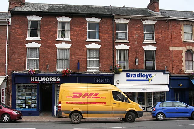 Two estate agents' shop fronts side by side on a high street, property cards displayed in the windows