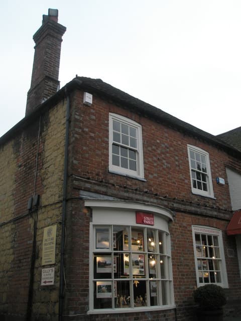 A lit estate agent's window at dusk on the ground floor of a brick building, filled with printed property listings