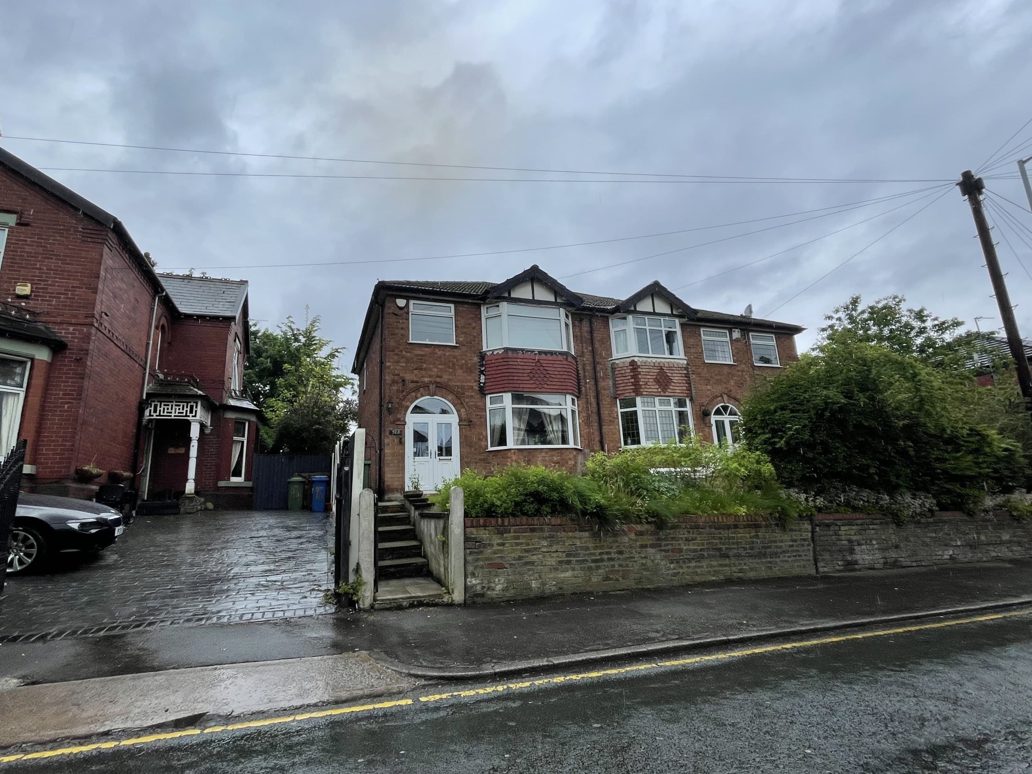 A pair of bay-fronted brick semi-detached houses behind a low garden wall on a wet residential street under grey cloud