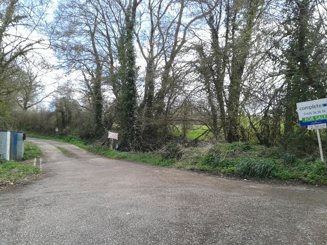 A house with a for sale sign at the end of its driveway on a quiet English street
