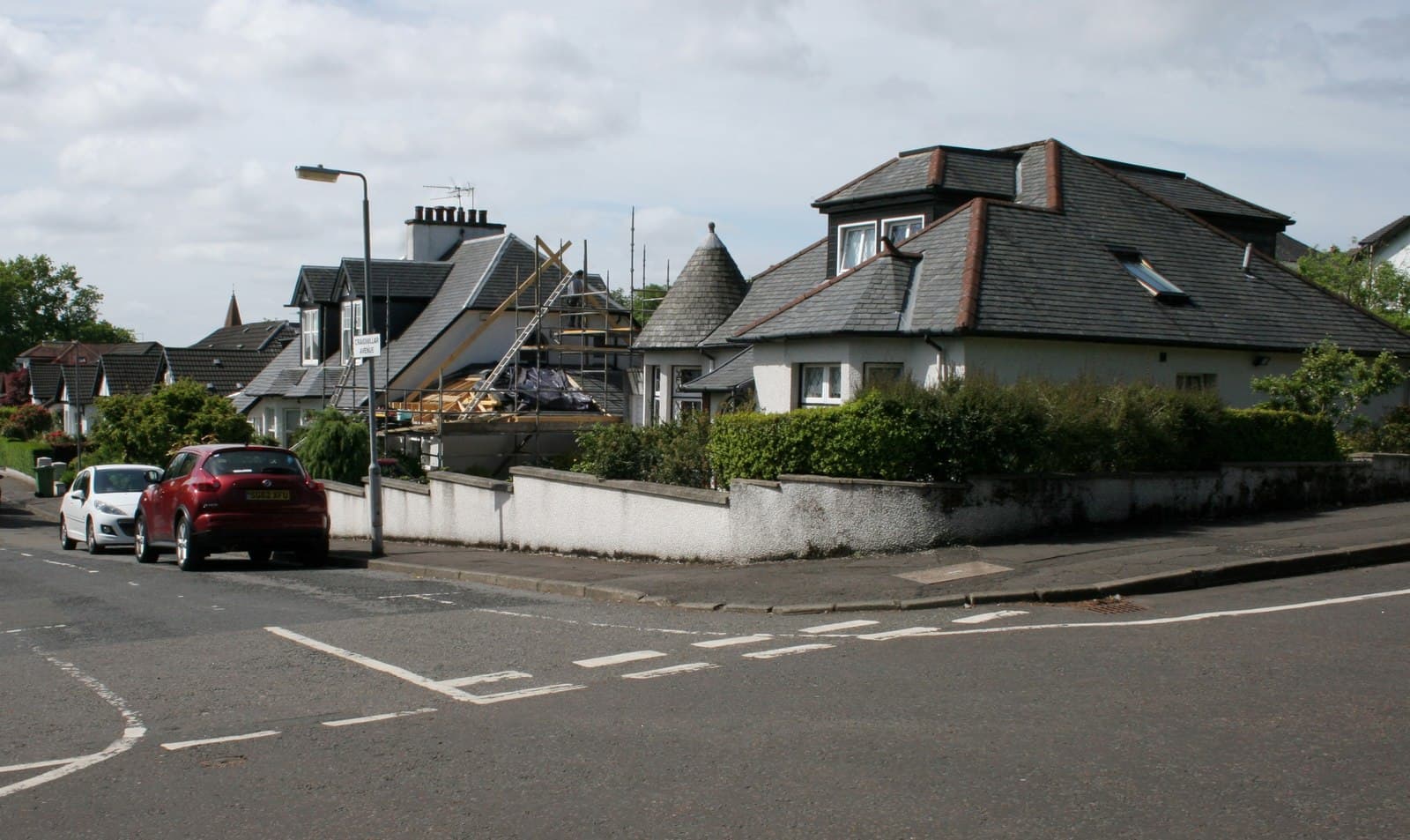 A suburban house with scaffolding over a part-built roof extension, seen from the road with neighbouring houses alongside