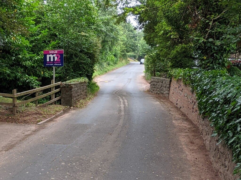 An estate agent's SOLD board outside a house on a rural lane
