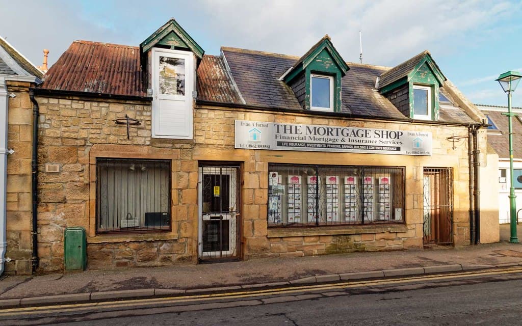 A mortgage broker's shopfront in a stone building on a village street, with property listings displayed in the window