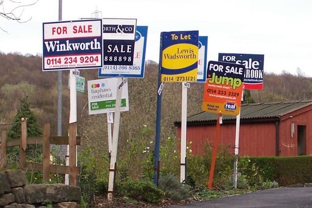 A cluster of estate agent for sale signs on one street, showing a crowded market
