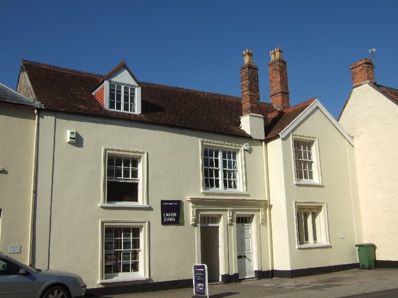 An estate agency office in a cream-painted period building on a sunny street, with a pavement board outside