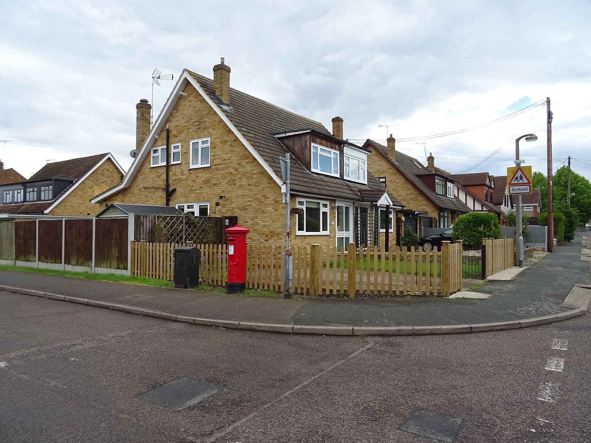 Brick chalet-style semi-detached houses with picket fences and a red post box on a street corner in Laindon, Basildon