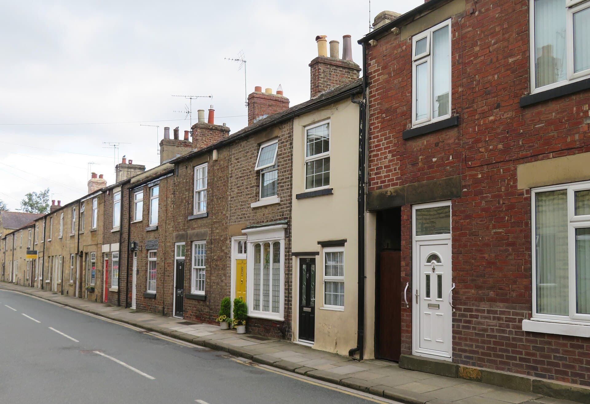 A row of brick and stone terraced houses with sash windows and chimney stacks along a quiet town street under a pale sky
