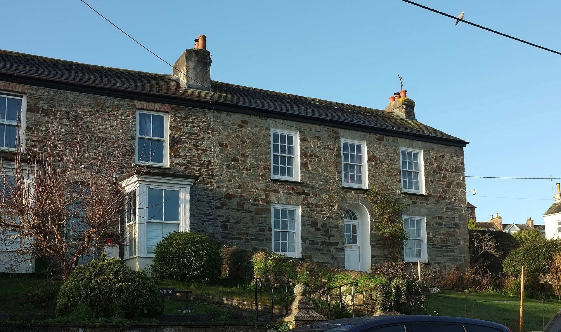 A pair of stone-built terraced houses with sash windows and a bay window on a sunny hillside in Cornwall